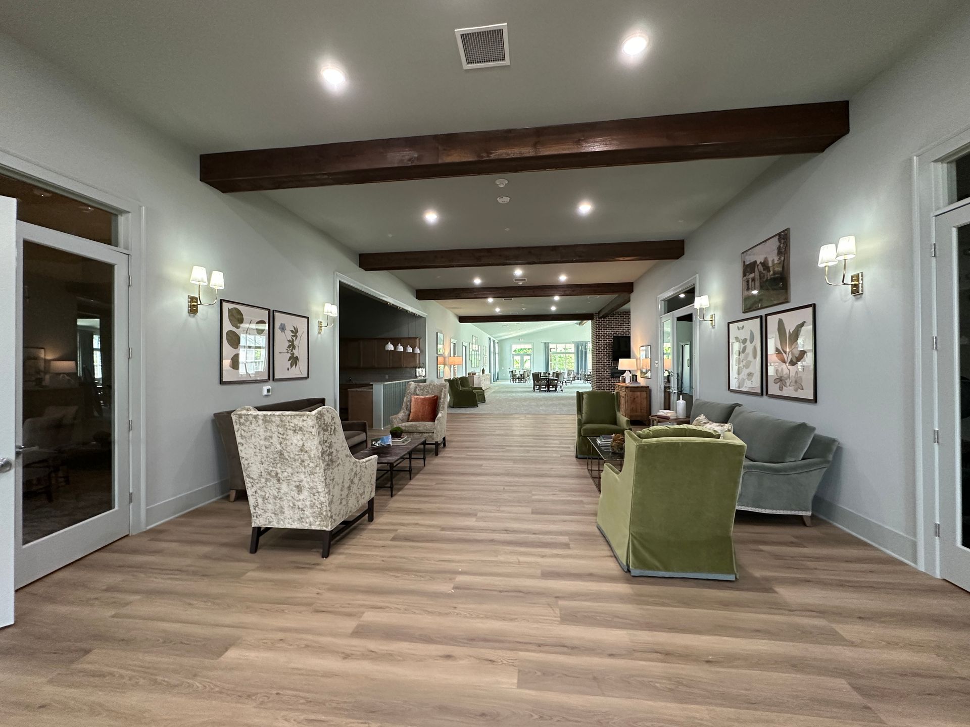 Modern lounge with wood floors, white walls, exposed beams, and upholstered chairs facing a large window.