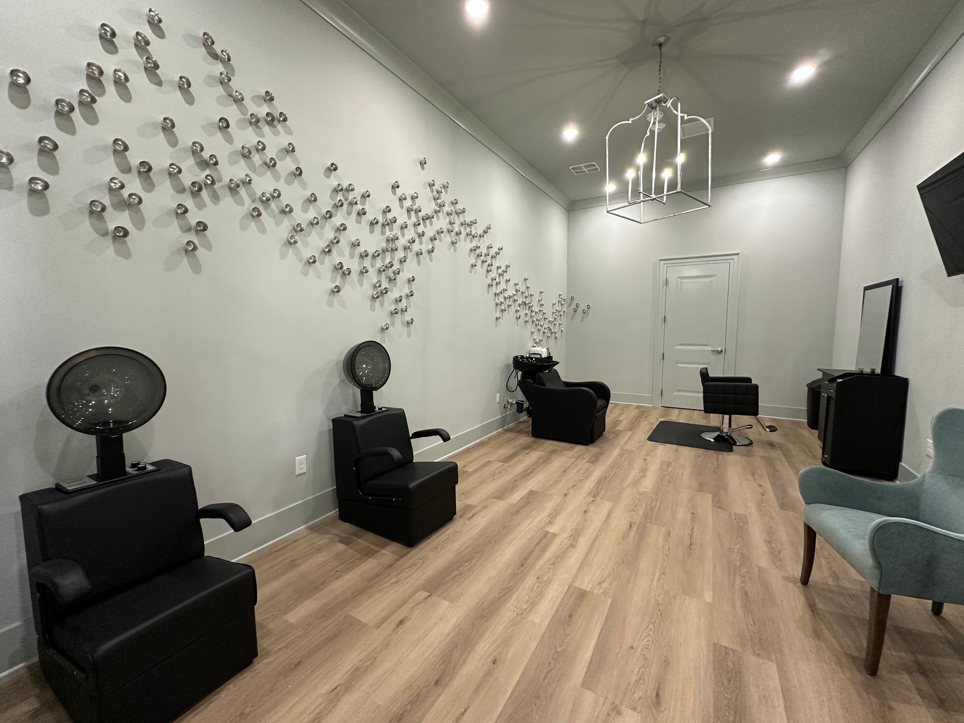 Modern salon with black styling chairs, wood floors, wall decor, and a ceiling light fixture