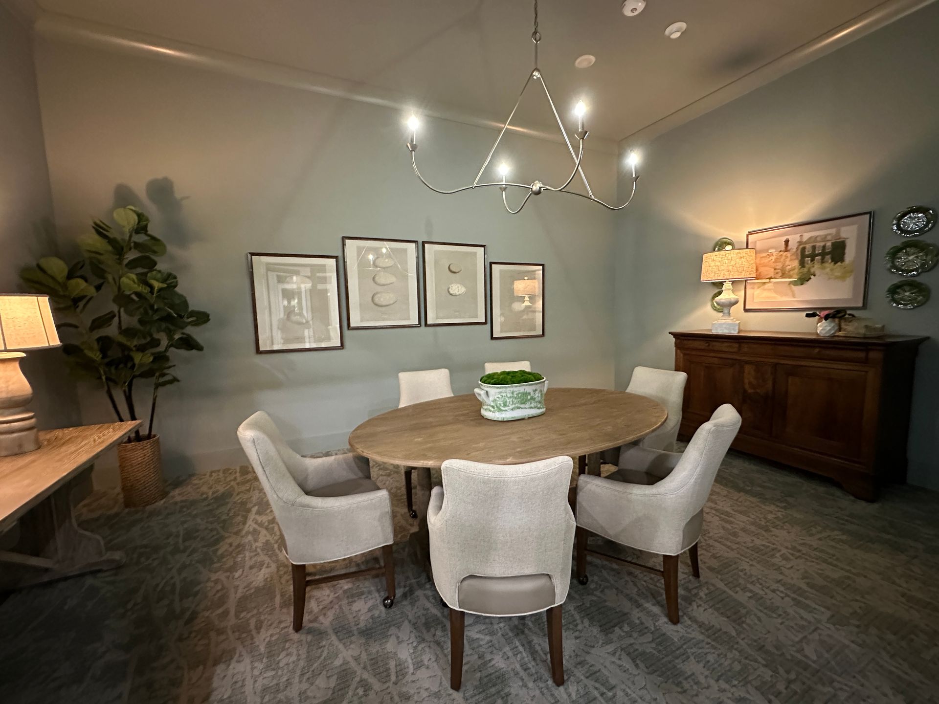 Elegant dining room with round wooden table, four cream chairs, wall art, and warm lamp lighting