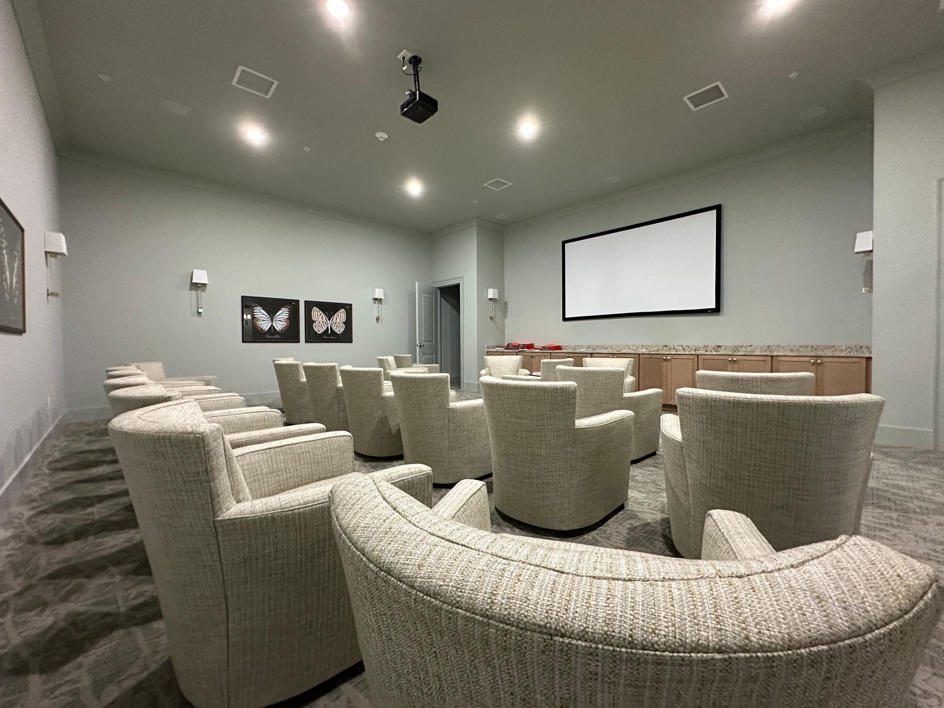 Modern theater room with gray lounge chairs, large projection screen, and wall art
