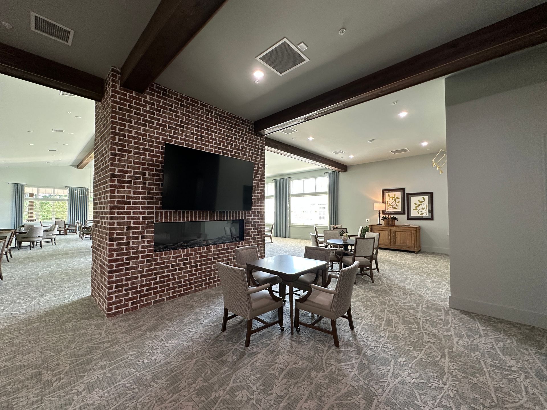 Modern living room with brick fireplace, wall-mounted TV, and dining table with chairs in an open floor plan.