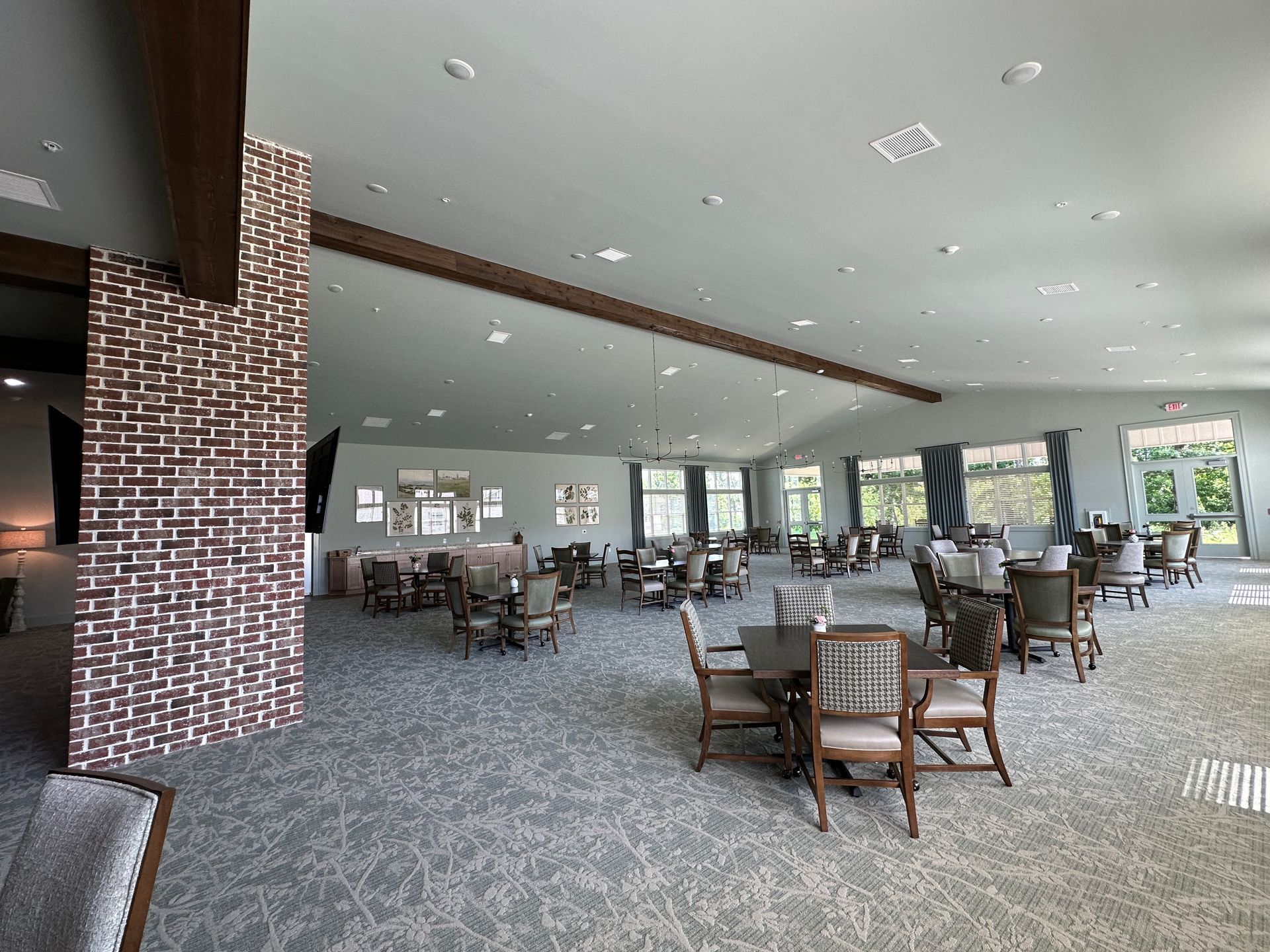 Spacious modern dining hall with round tables, chairs, and large windows overlooking greenery
