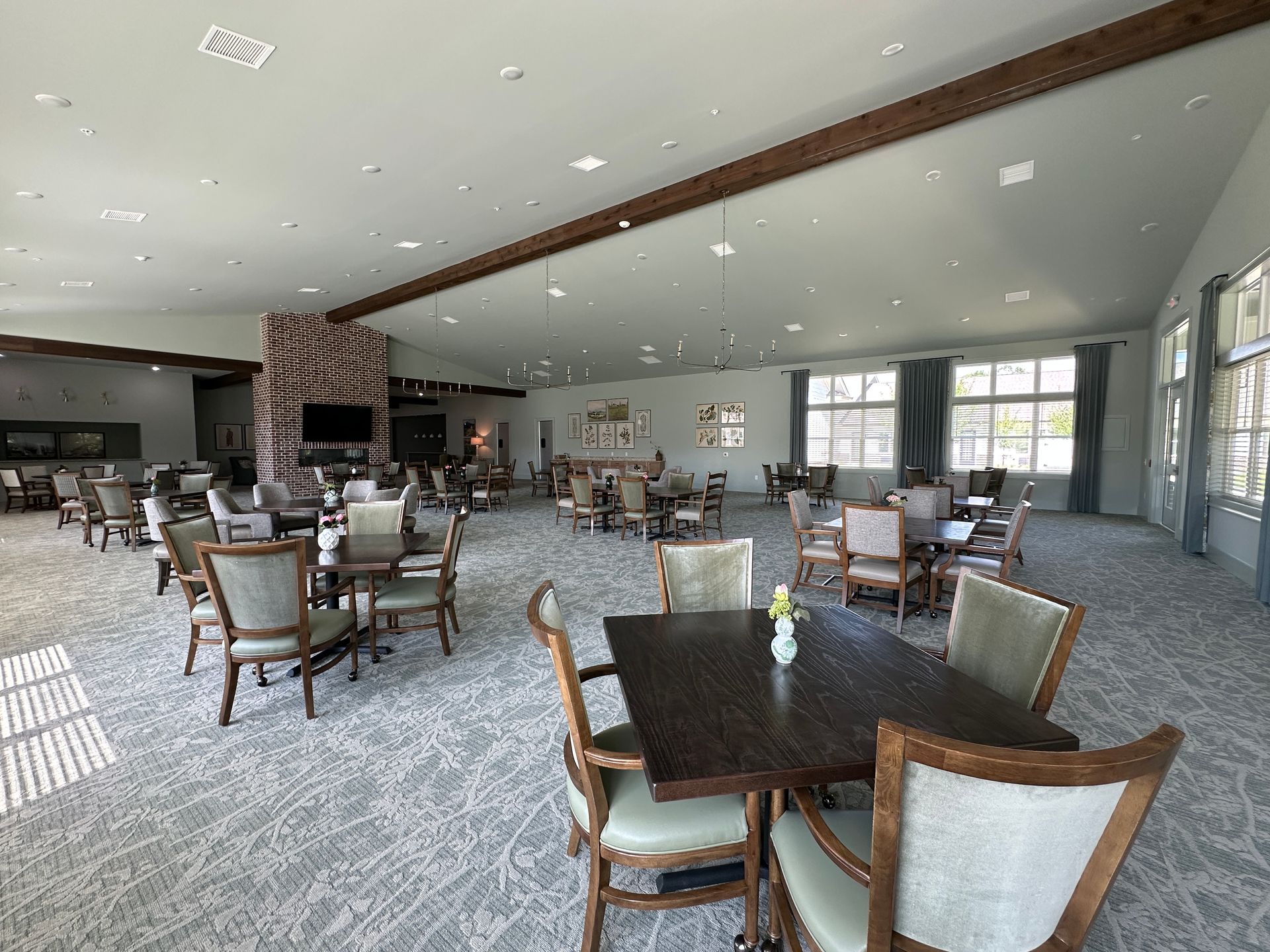 Large dining hall with scattered tables and chairs, carpeted floor, and windows along the right wall
