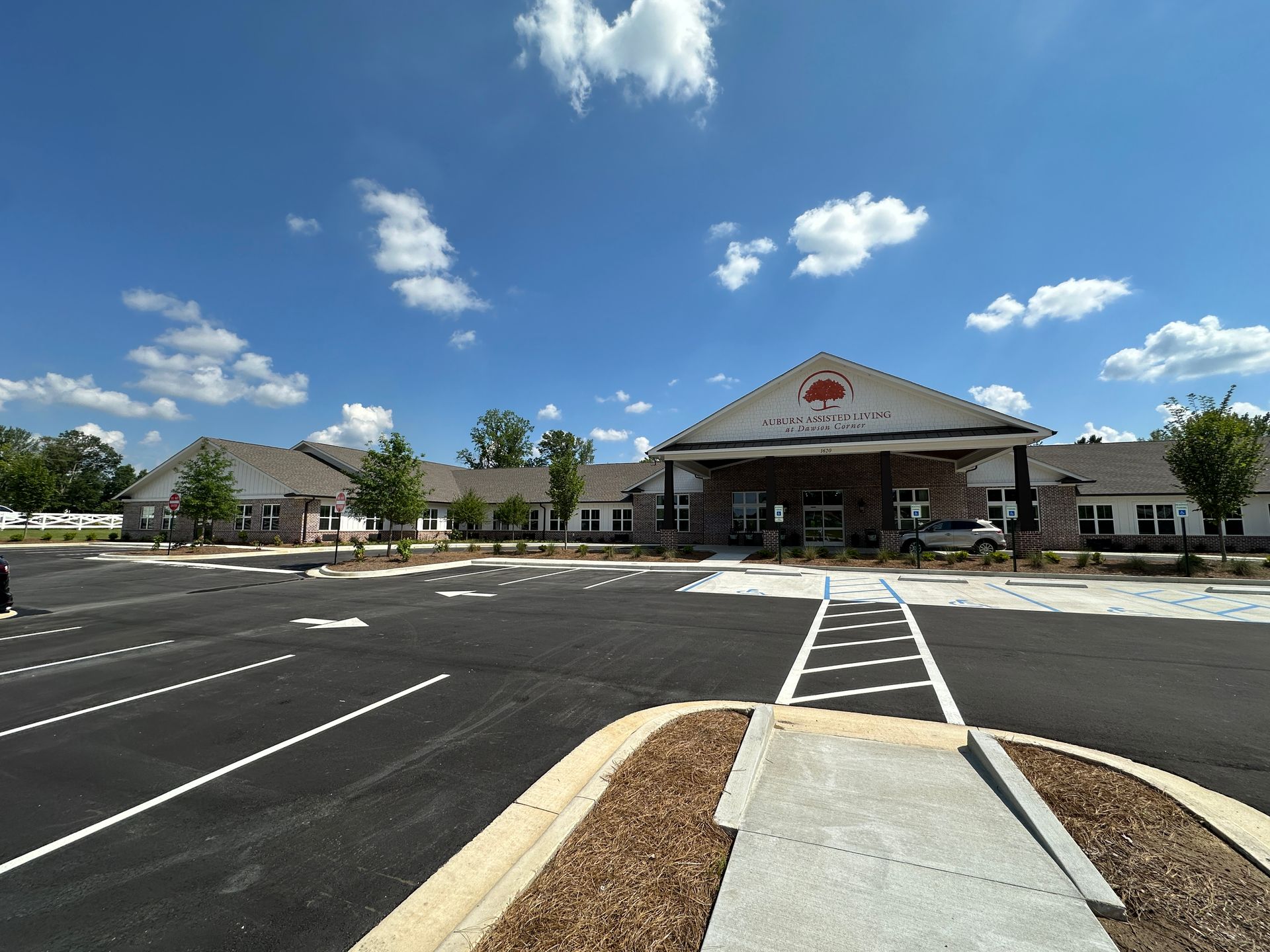 Wide parking lot leading to a brick civic building under a bright blue sky with scattered clouds.