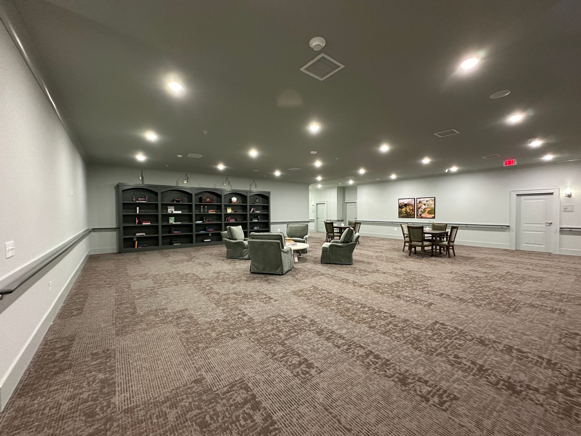 Spacious carpeted meeting room with tables, chairs, wall shelving, and recessed ceiling lights