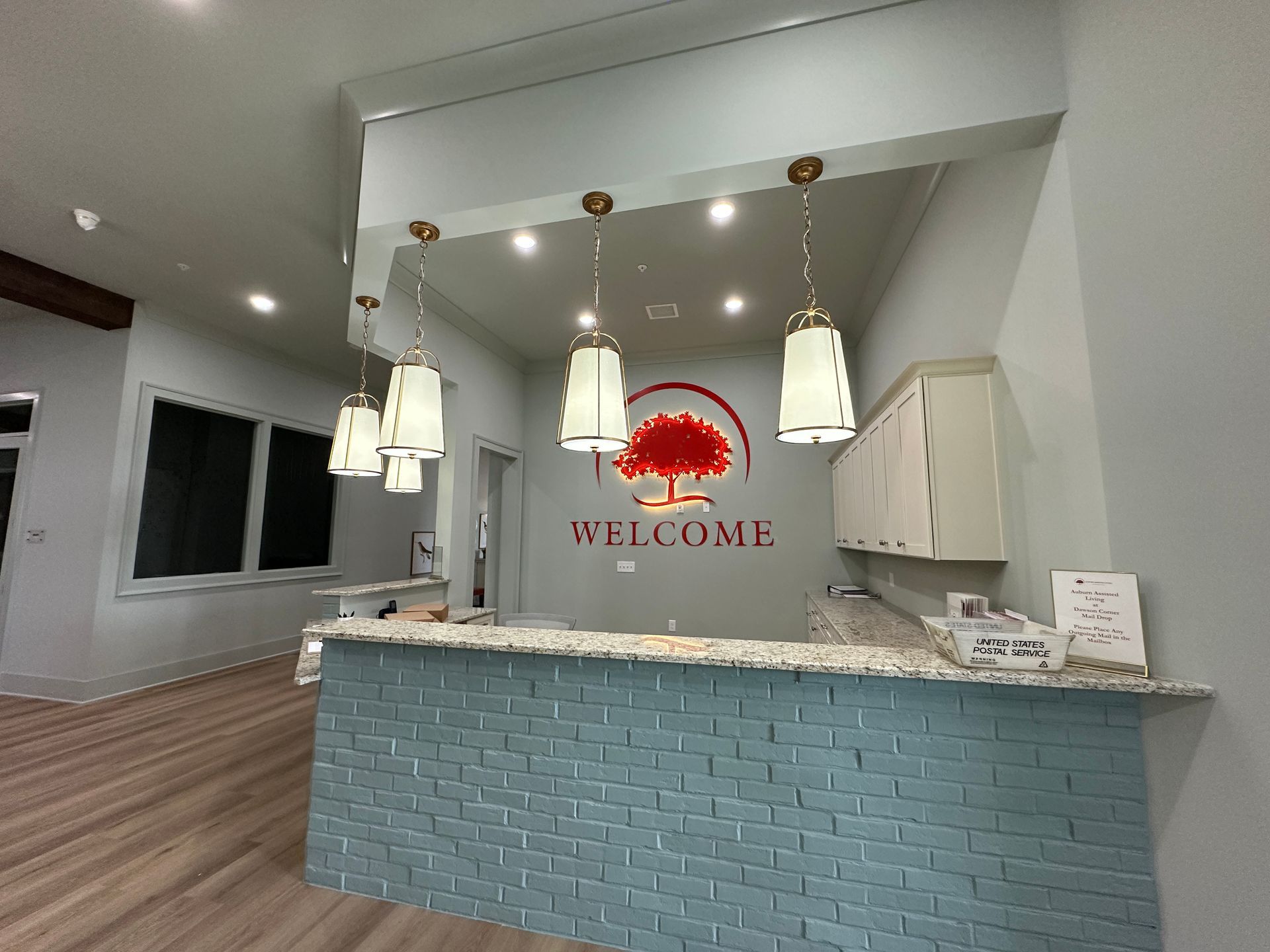 Bright lobby reception desk with blue tile, hanging pendant lights, and a “WELCOME” sign on the back wall