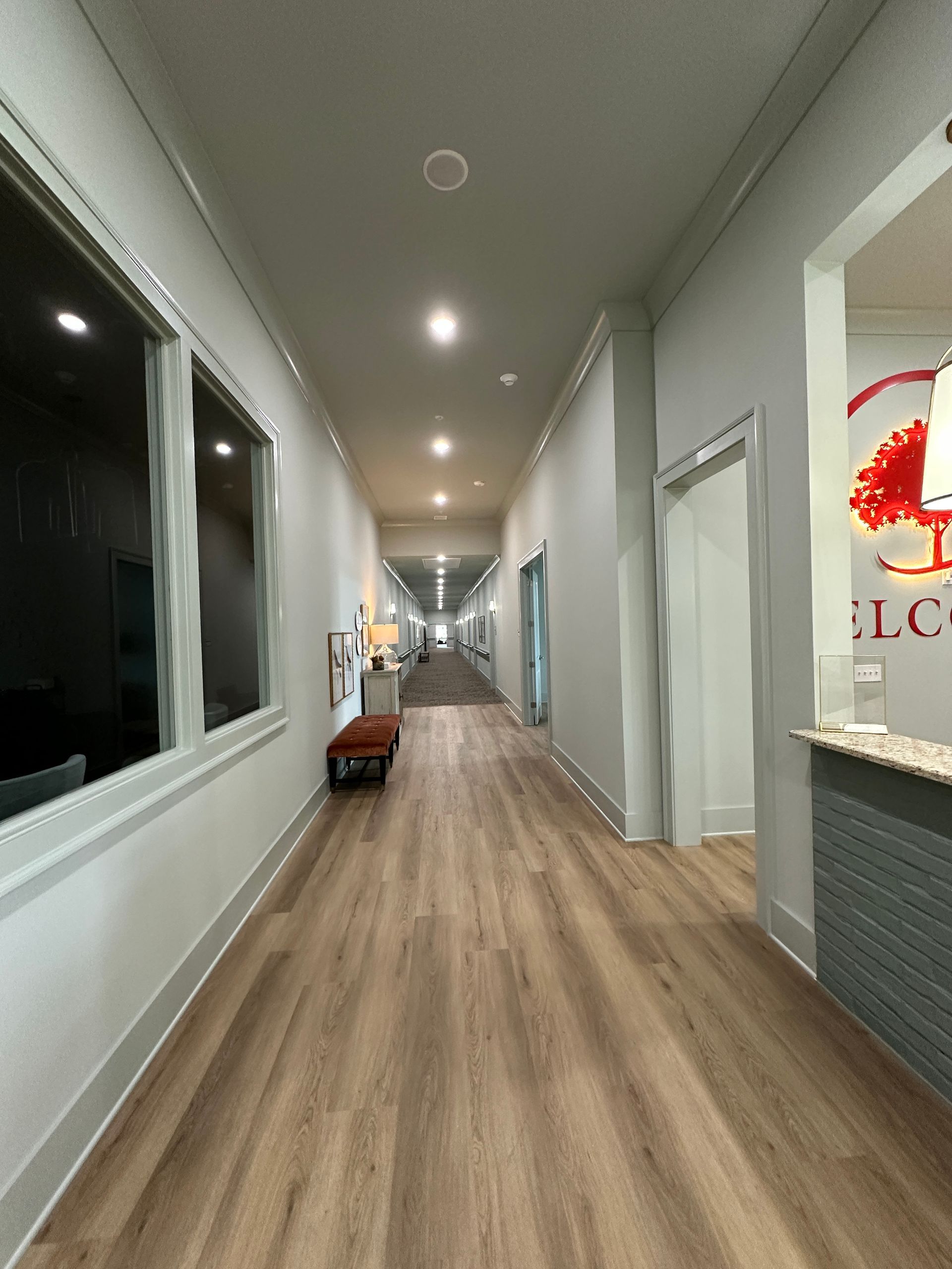 Narrow office hallway with wood flooring, white walls, windows, and recessed ceiling lights