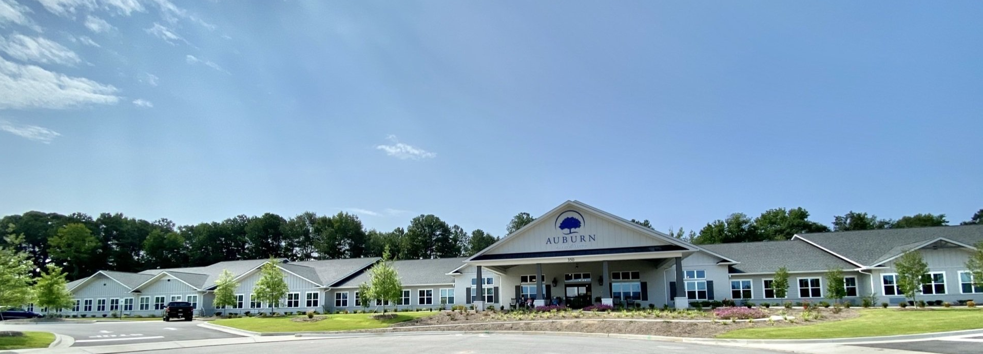 A large white building with a blue roof is surrounded by trees on a sunny day.