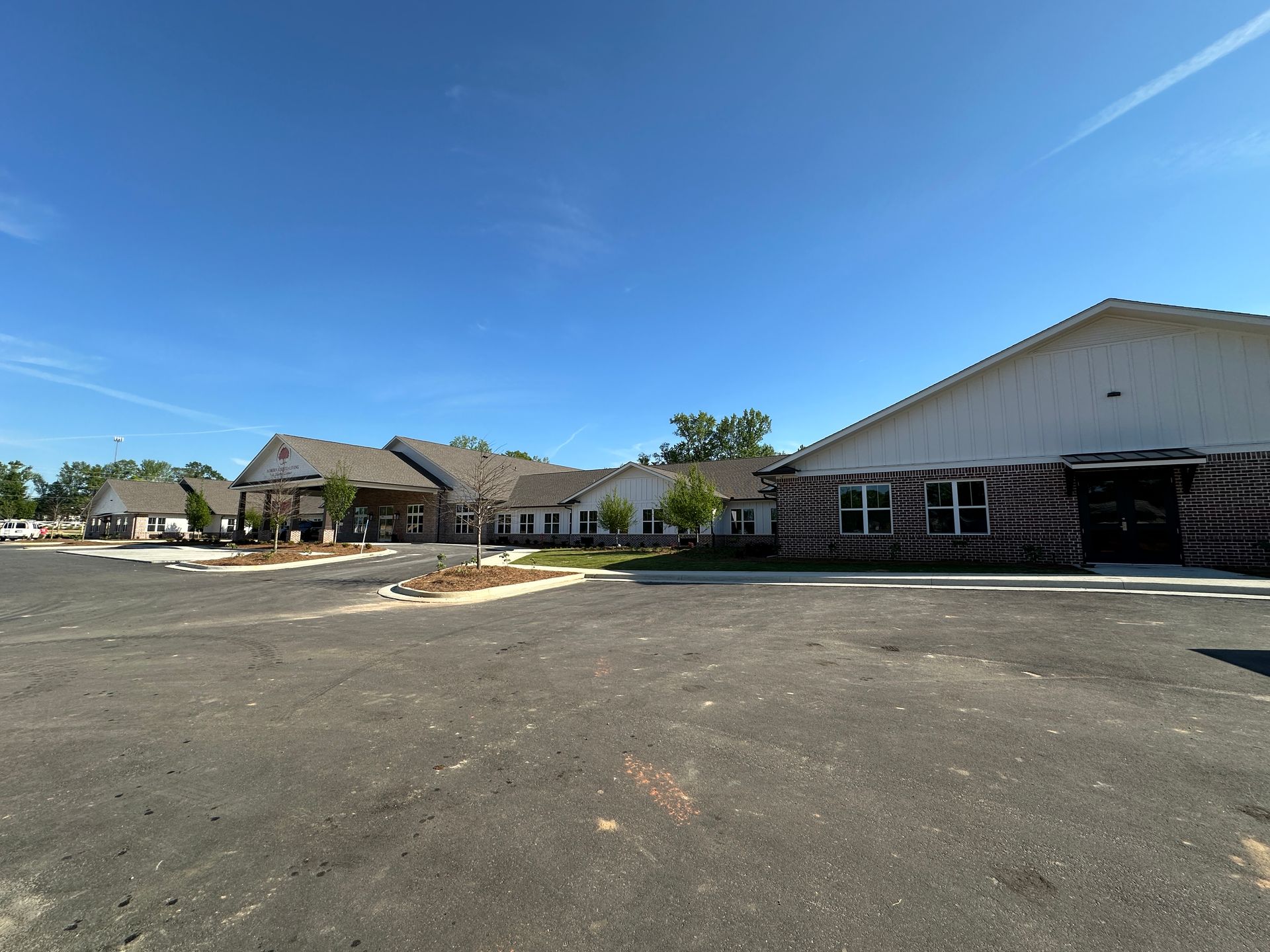 A low, modern single-story complex with a mix of brick and white siding under a clear blue sky, next to a large parking lot.