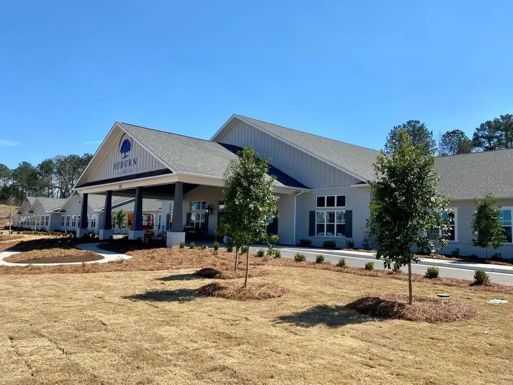New assisted living building with gabled roof and covered entrance, surrounded by young trees under a clear blue sky