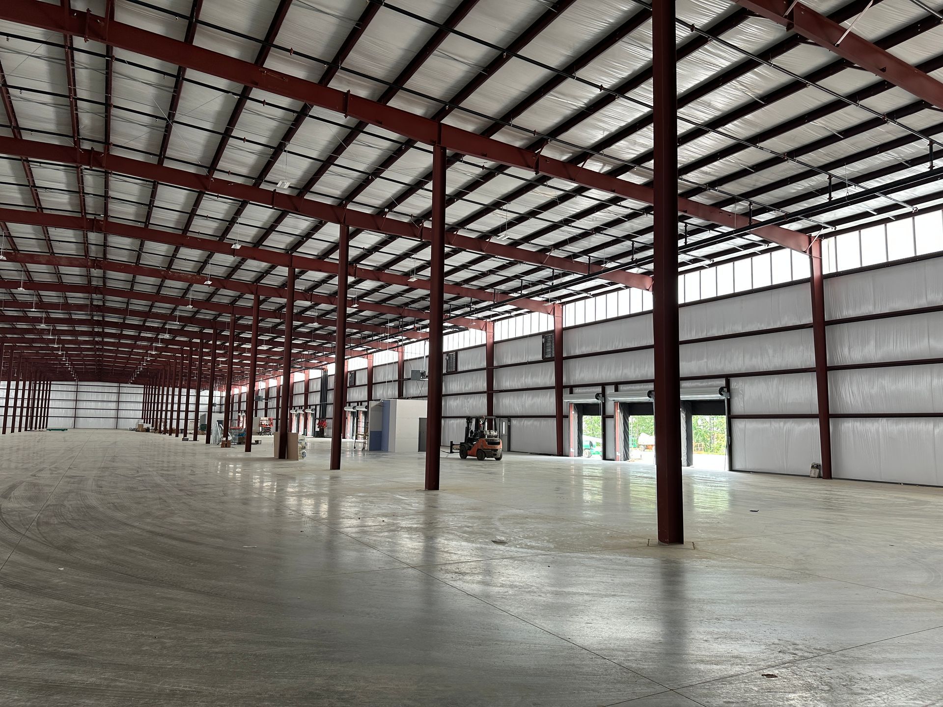 Empty industrial warehouse with a high metal roof, red support columns, and a concrete floor