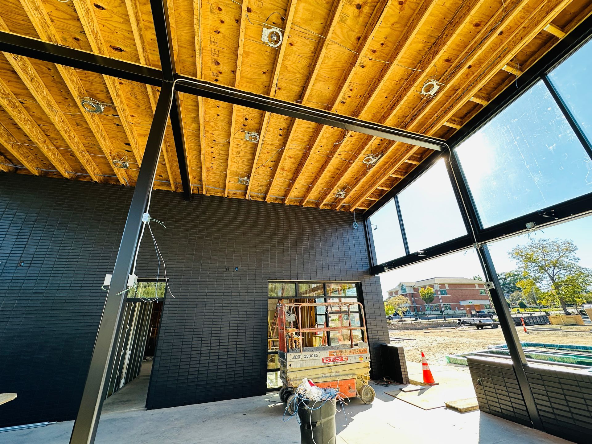 Interior of a construction site with exposed wood ceiling, dark walls, and large windows overlooking outside.