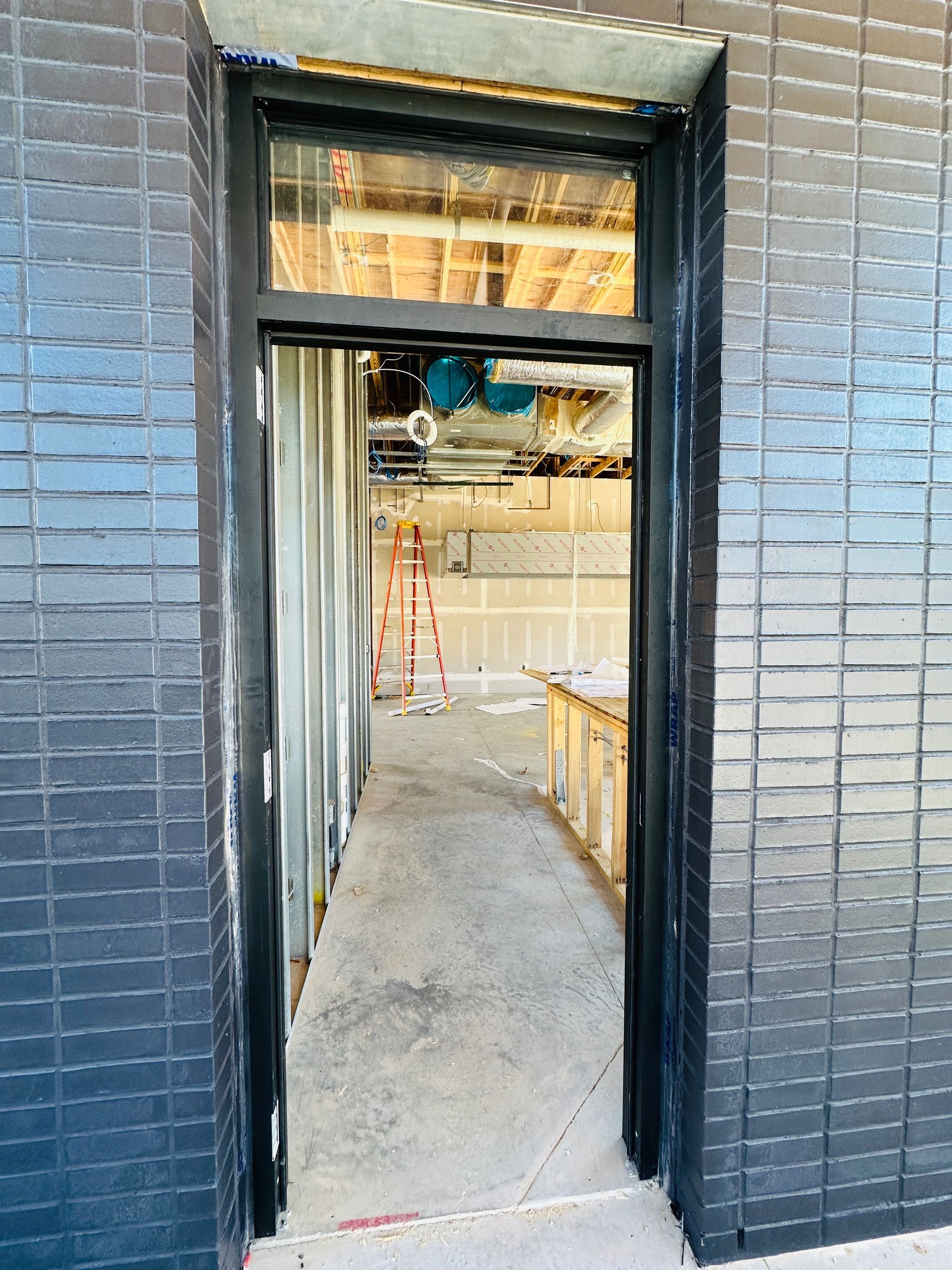Open doorway into a construction site with unfinished walls, concrete floor, and exposed ceiling beams