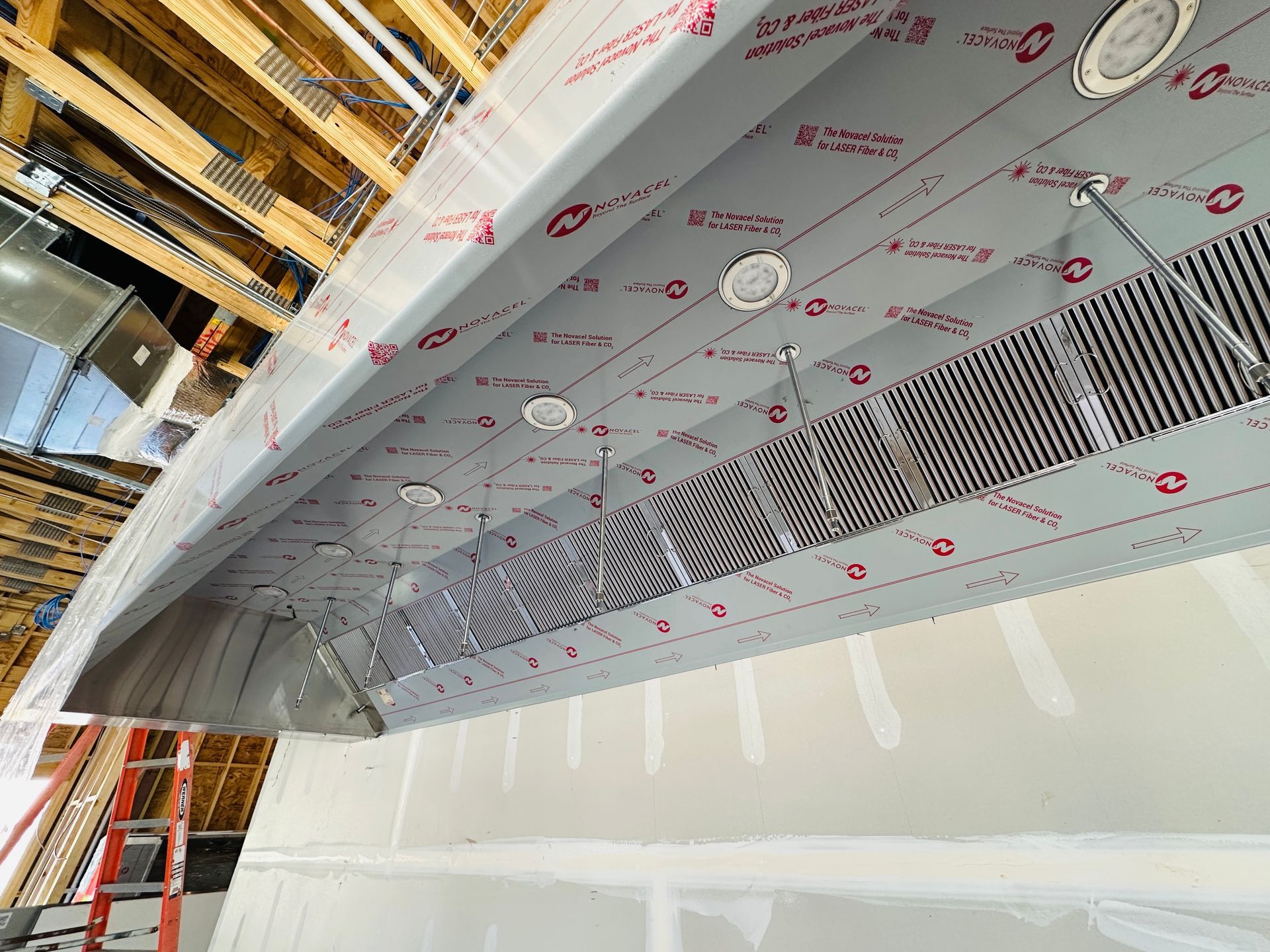 Interior construction site with suspended ductwork, ceiling panels, and scaffolding.
