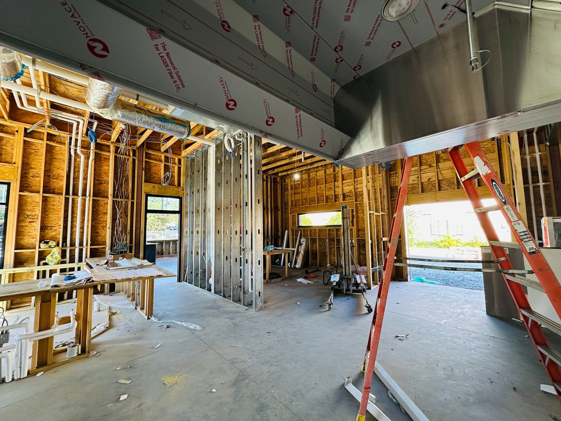 Interior of a restaurant under construction with exposed framing, insulation, and a red ladder near a bright doorway