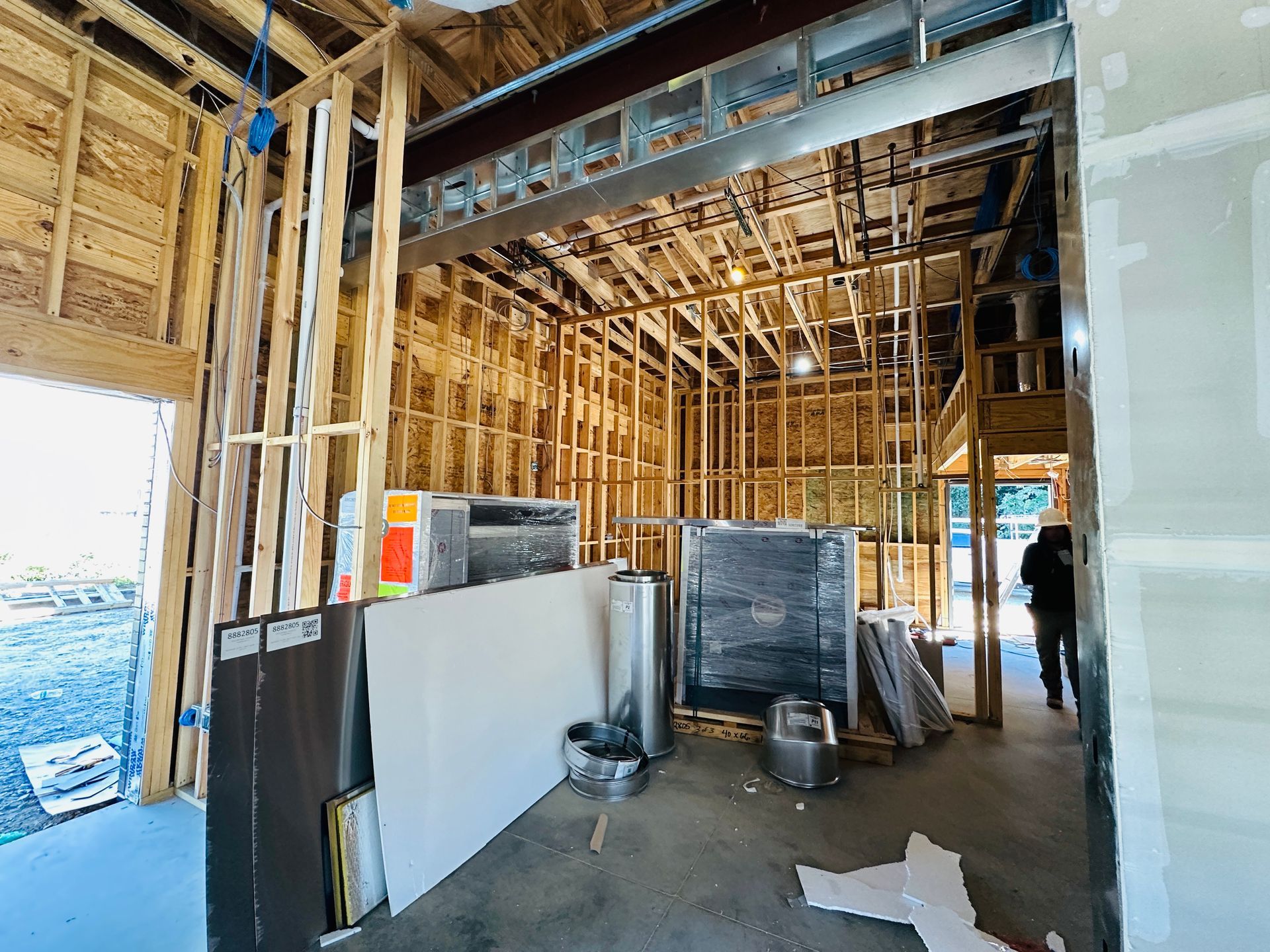 Interior of a restaurant under construction with exposed framing, drywall sheets, and construction equipment.