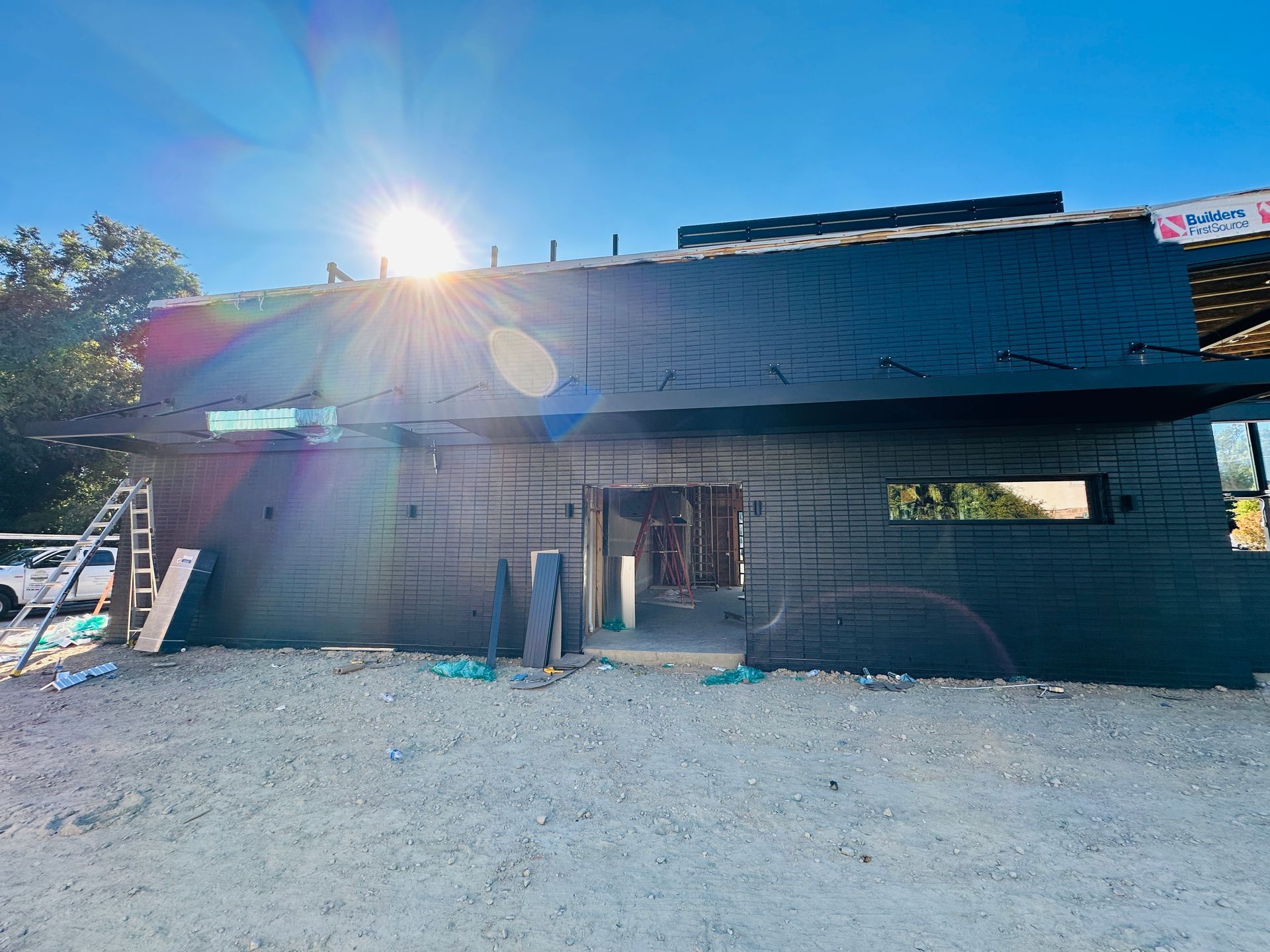 Small black building under construction with a sunlit roof and gravel foreground.