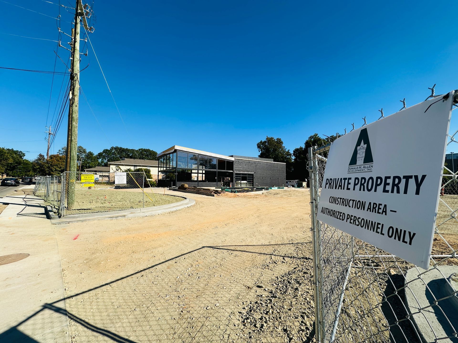 Rural dirt lot with a white “Private Property” sign, utility poles, and buildings under a blue sky
