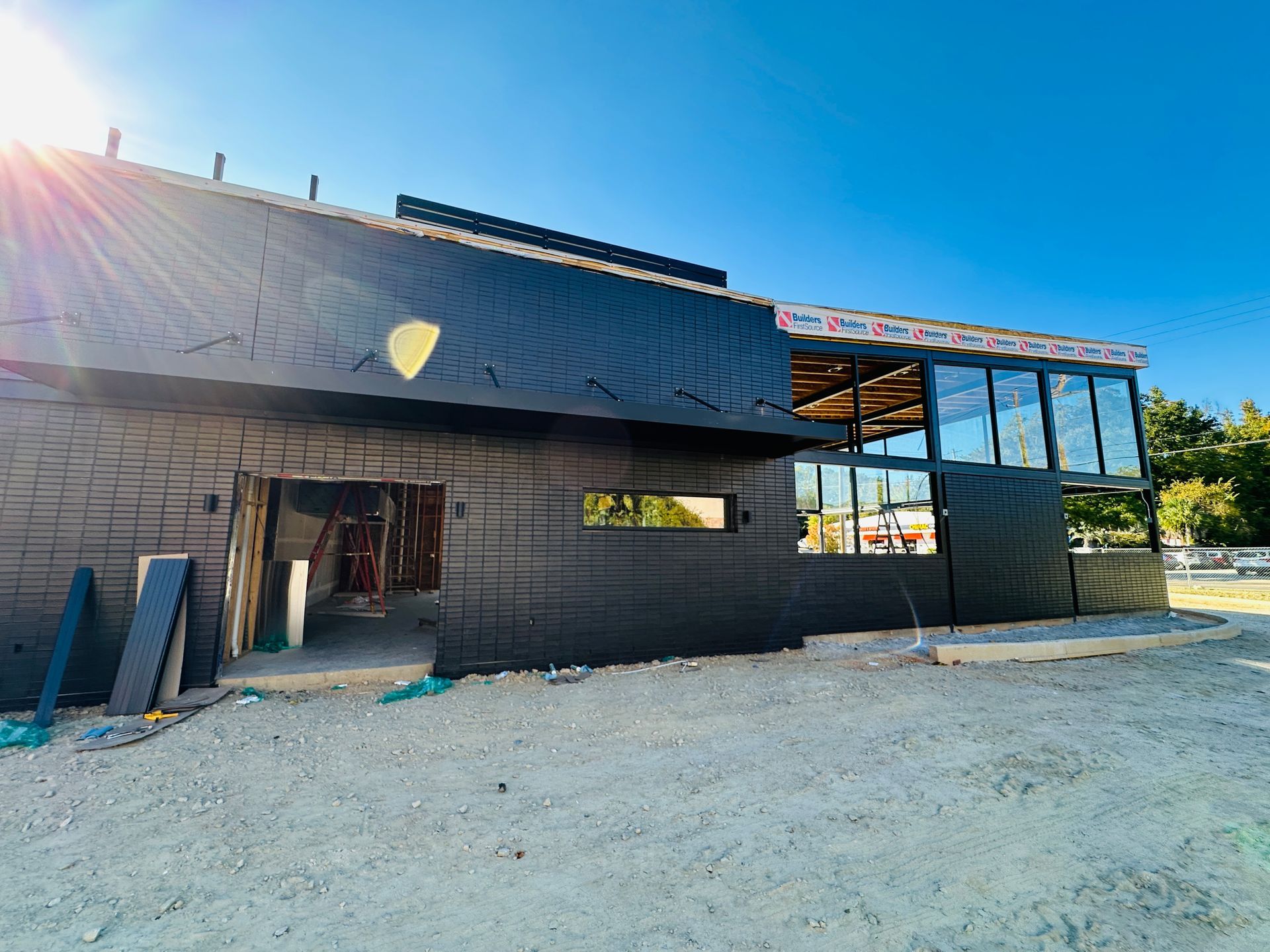 Black building under construction with unfinished roof and open side on a gravel lot in bright sunlight