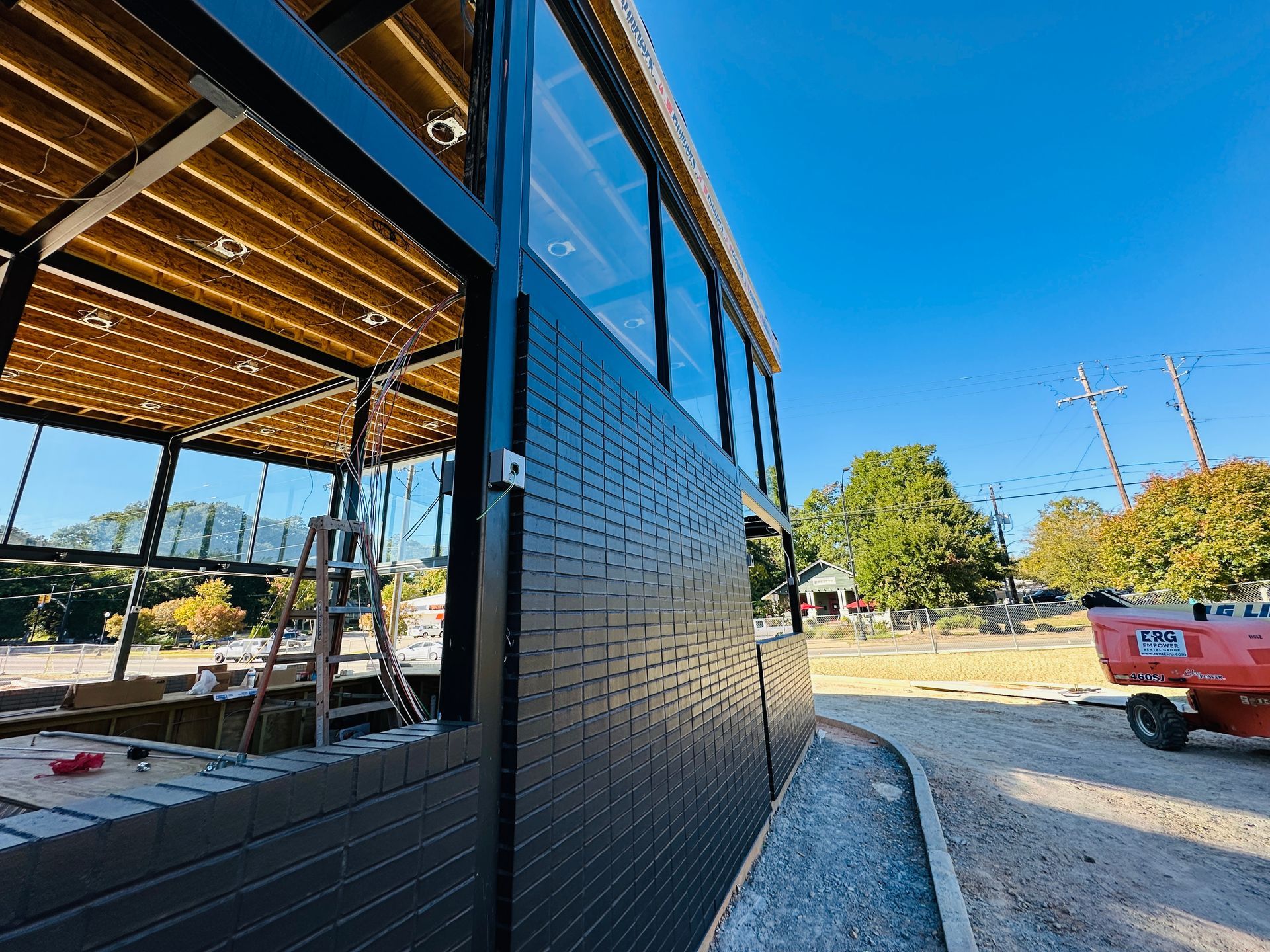 Black brick building under construction with blue trim and a red truck on a sunny day