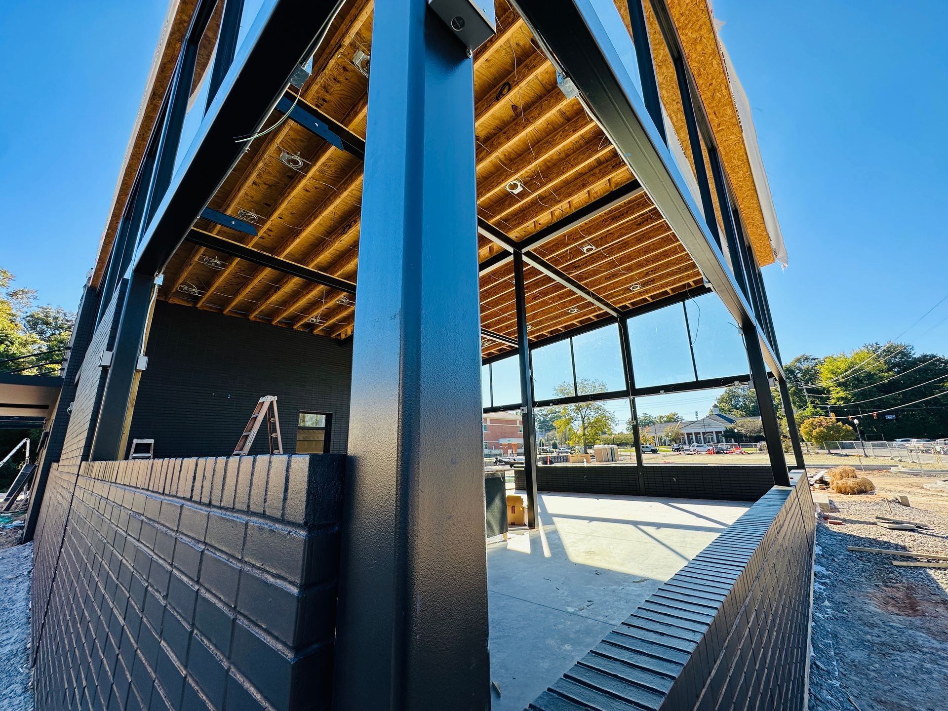 Modern building with black metal columns, wood ceiling, and open patio under a blue sky.