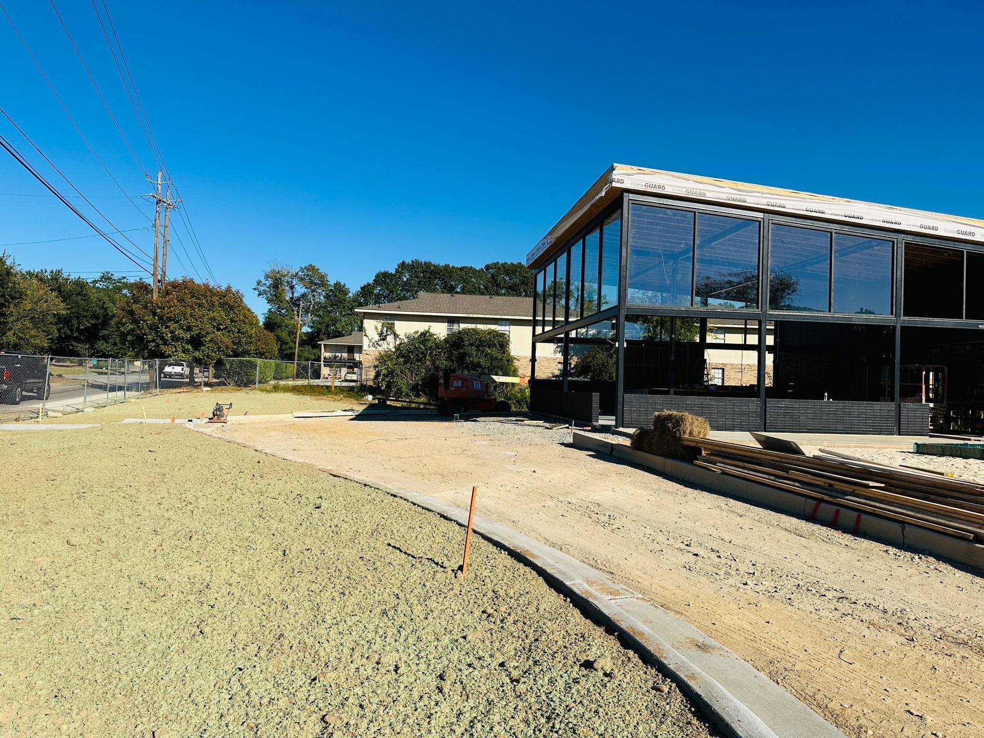Modern glass building beside a gravel path and open grassy area under a clear blue sky