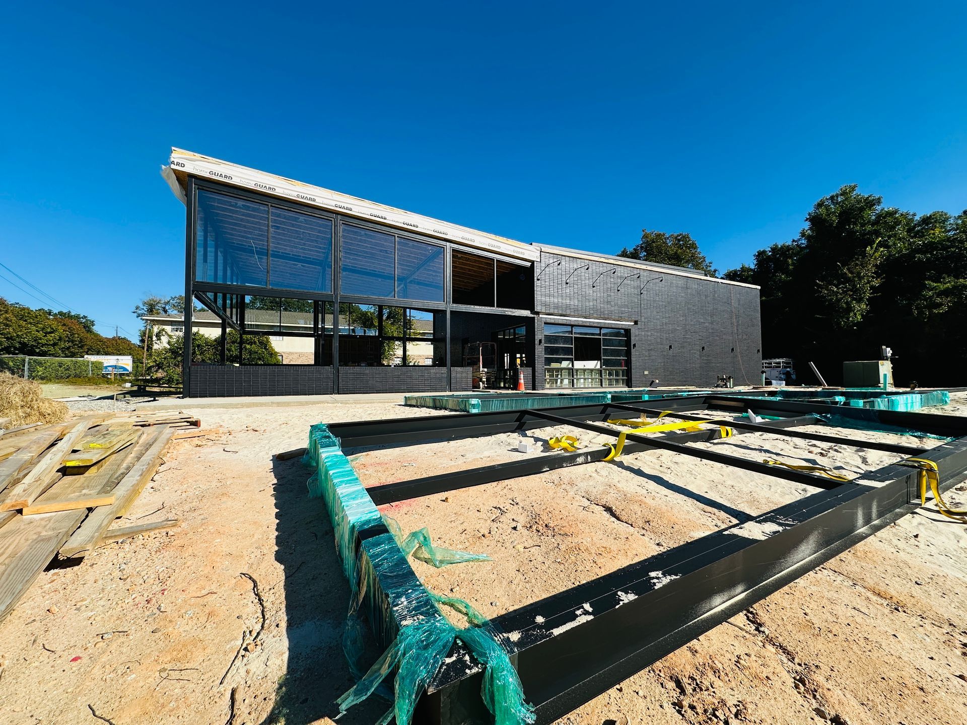 Modern building under construction with exposed framing and sand in the foreground under a clear blue sky