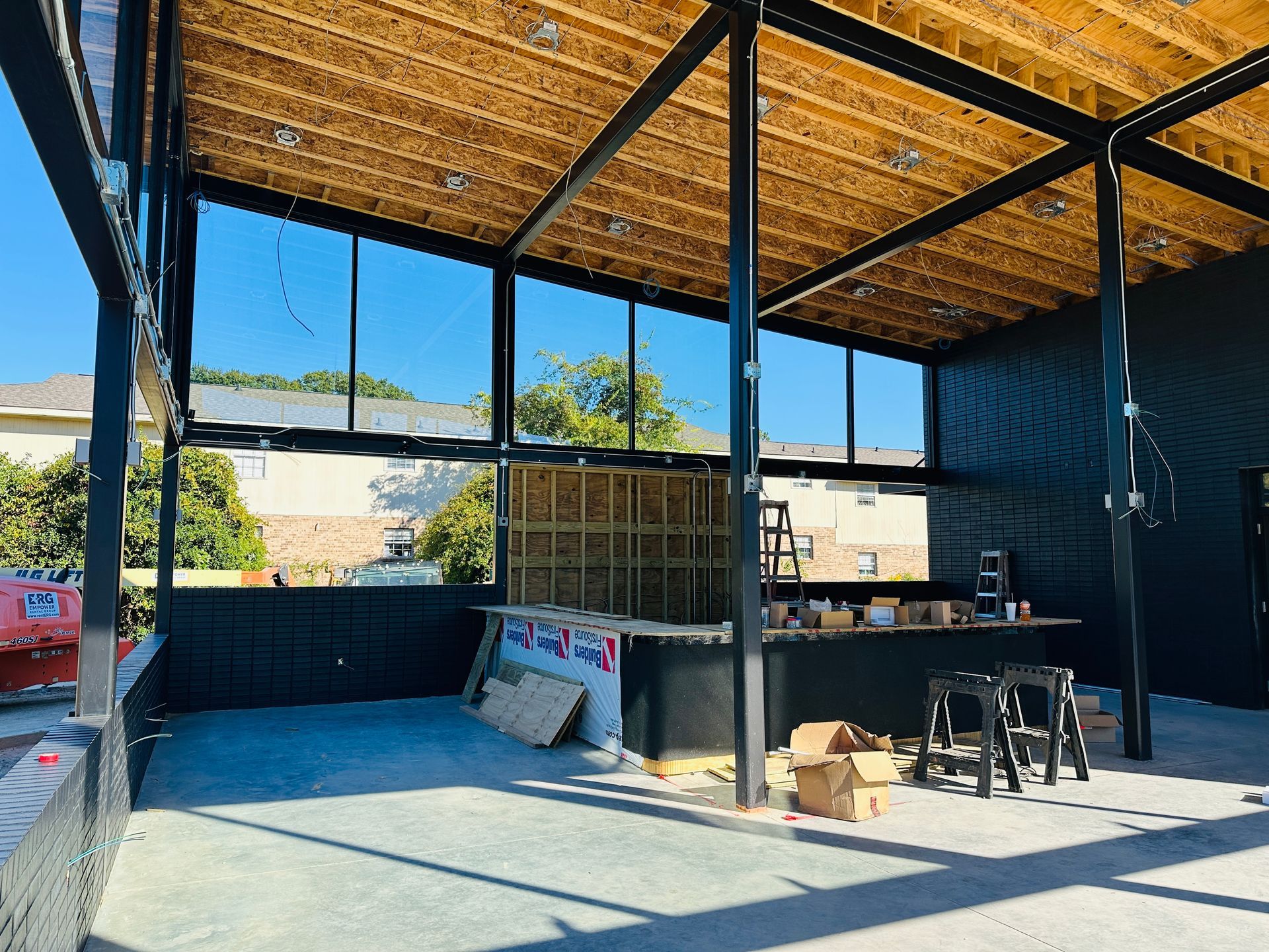 Open-air construction workspace with steel frame, wood roof, and tools on a concrete floor