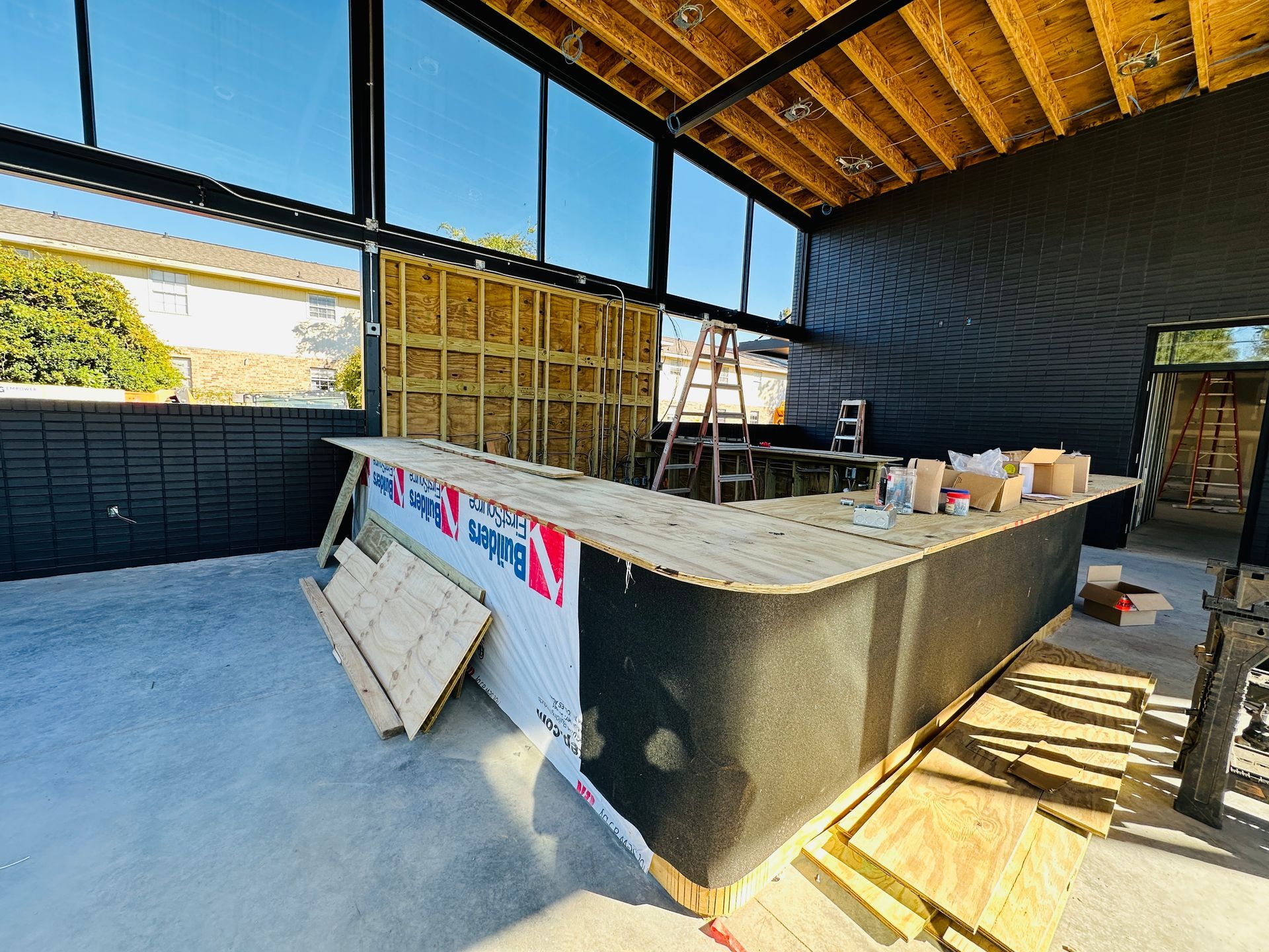 Partially built outdoor bar with concrete counter, exposed framing, and construction materials in a covered patio area