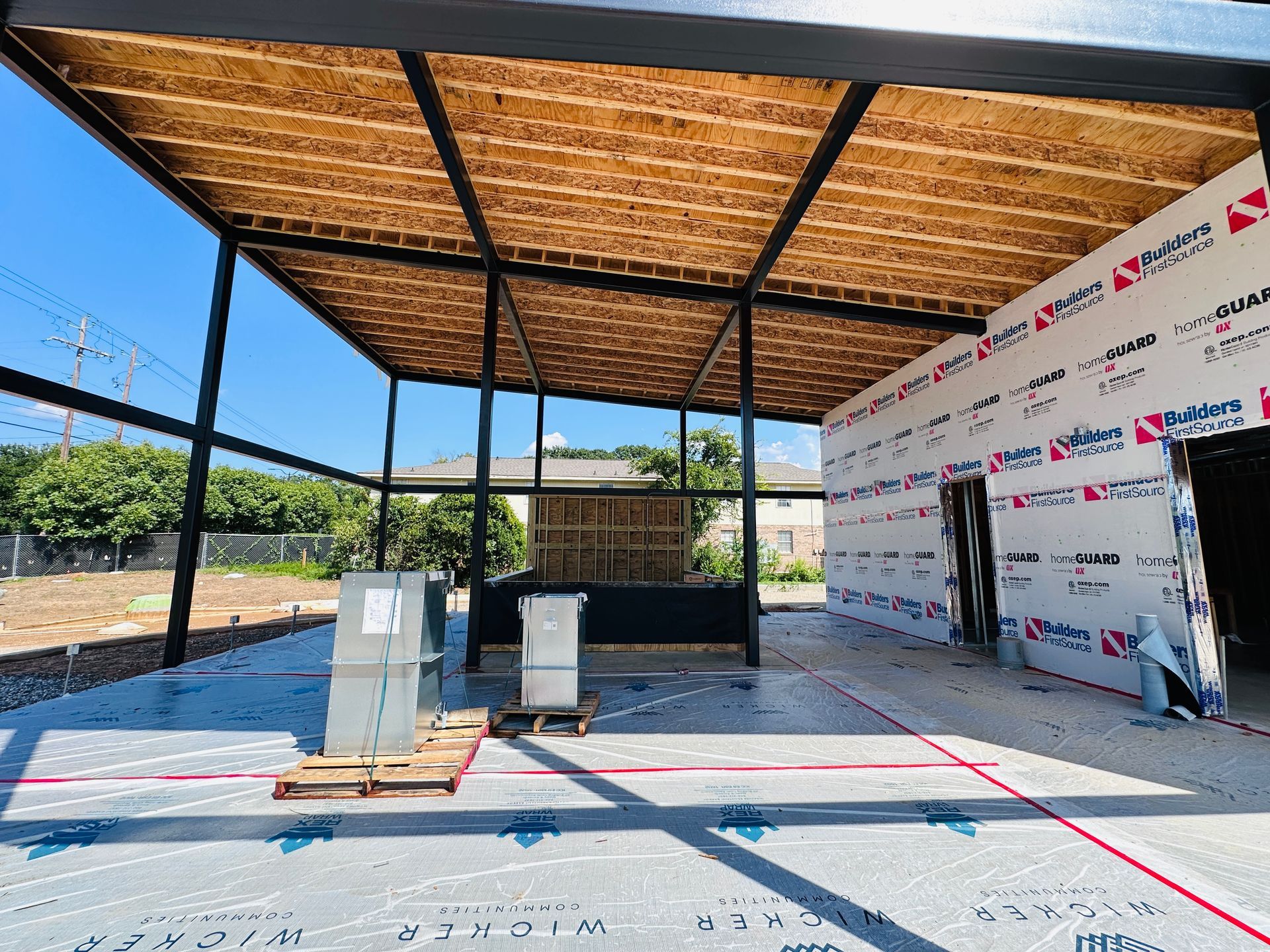 Open-air pavilion under construction with a wood roof, metal frame, and equipment on a concrete slab.