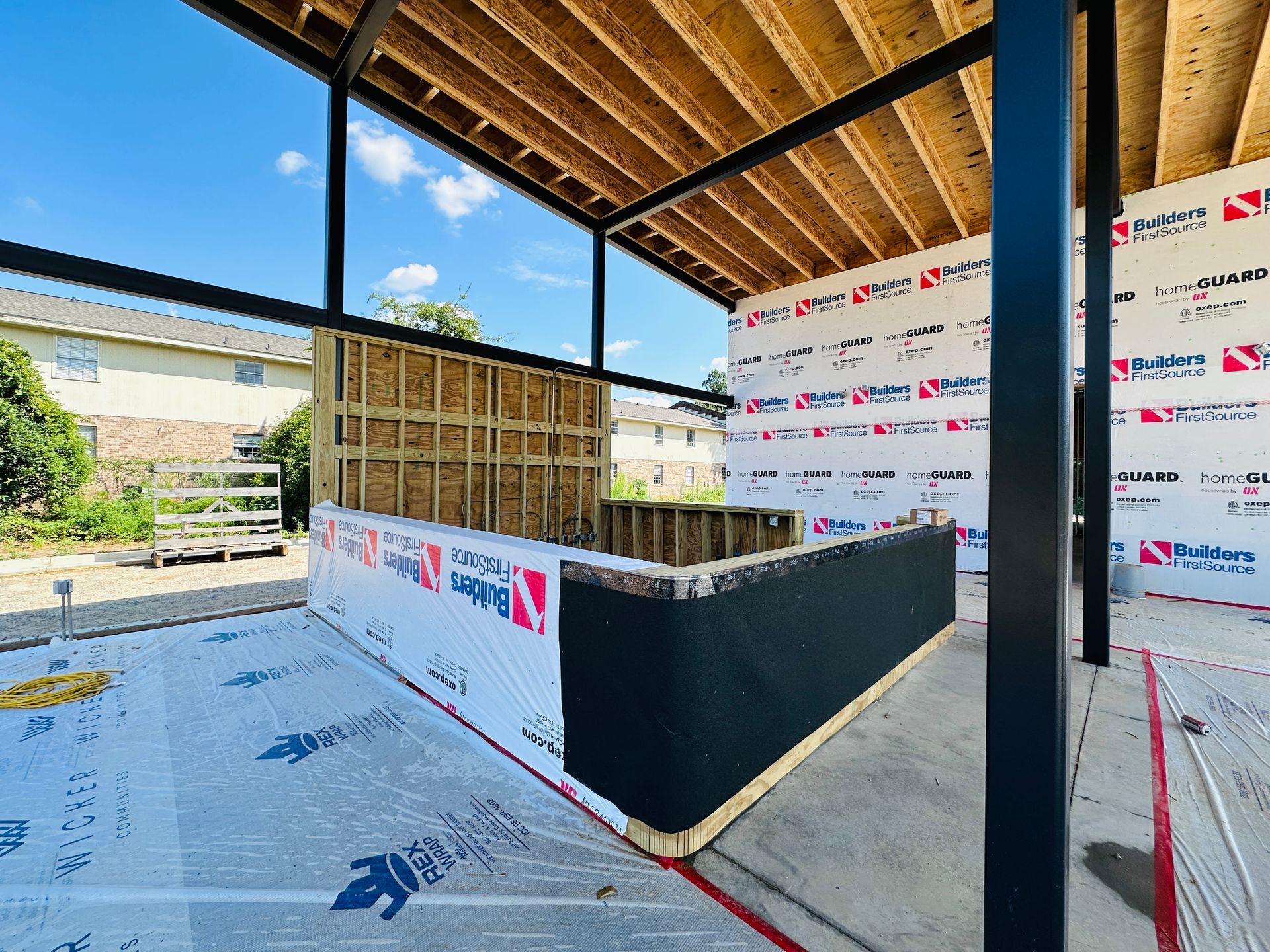 Partially built interior with exposed wooden roof, black walls, and construction wrap in a covered outdoor area