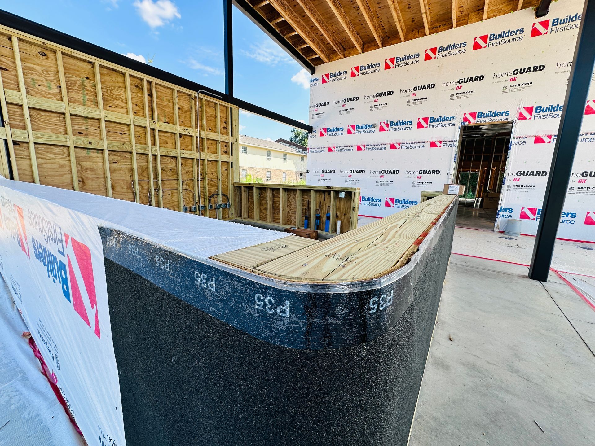 Construction site interior with black-topped curved wall and exposed framing under a roof￼