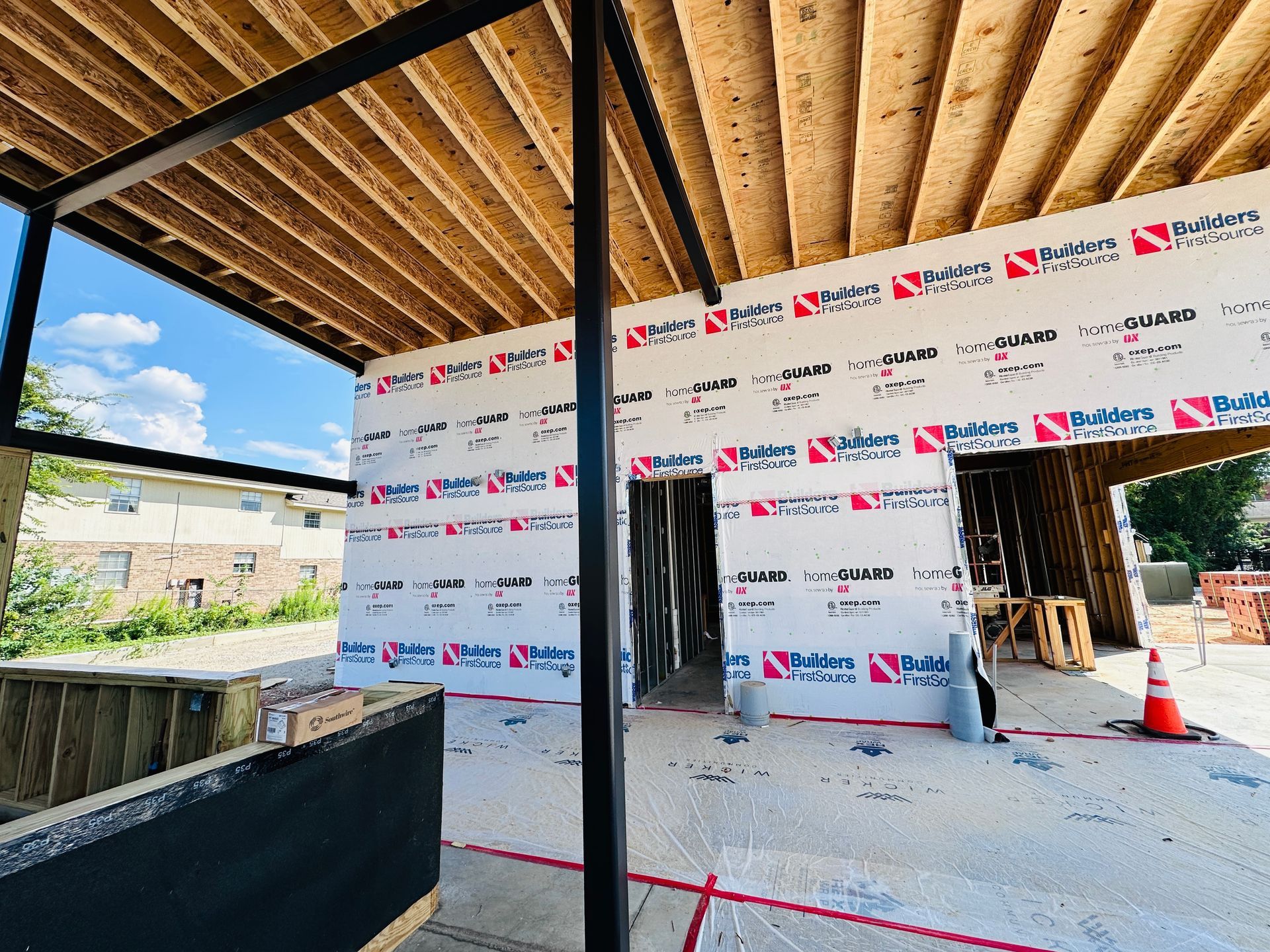 Partially built house exterior with white wrap, exposed framing, and a concrete slab under construction