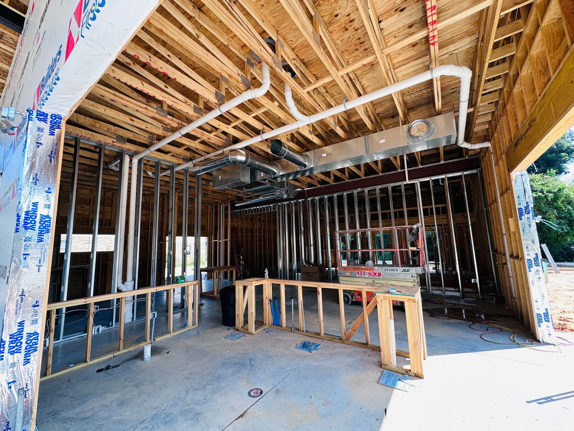 Interior of a house under construction with exposed wood framing, piping, and temporary wooden supports.
