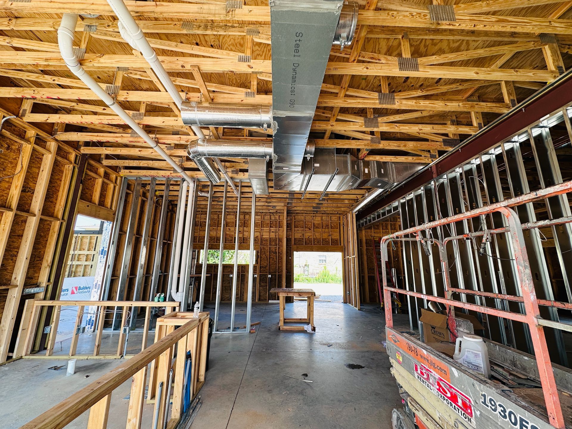 Unfinished house interior with exposed wooden framing, ductwork, and temporary stairs.