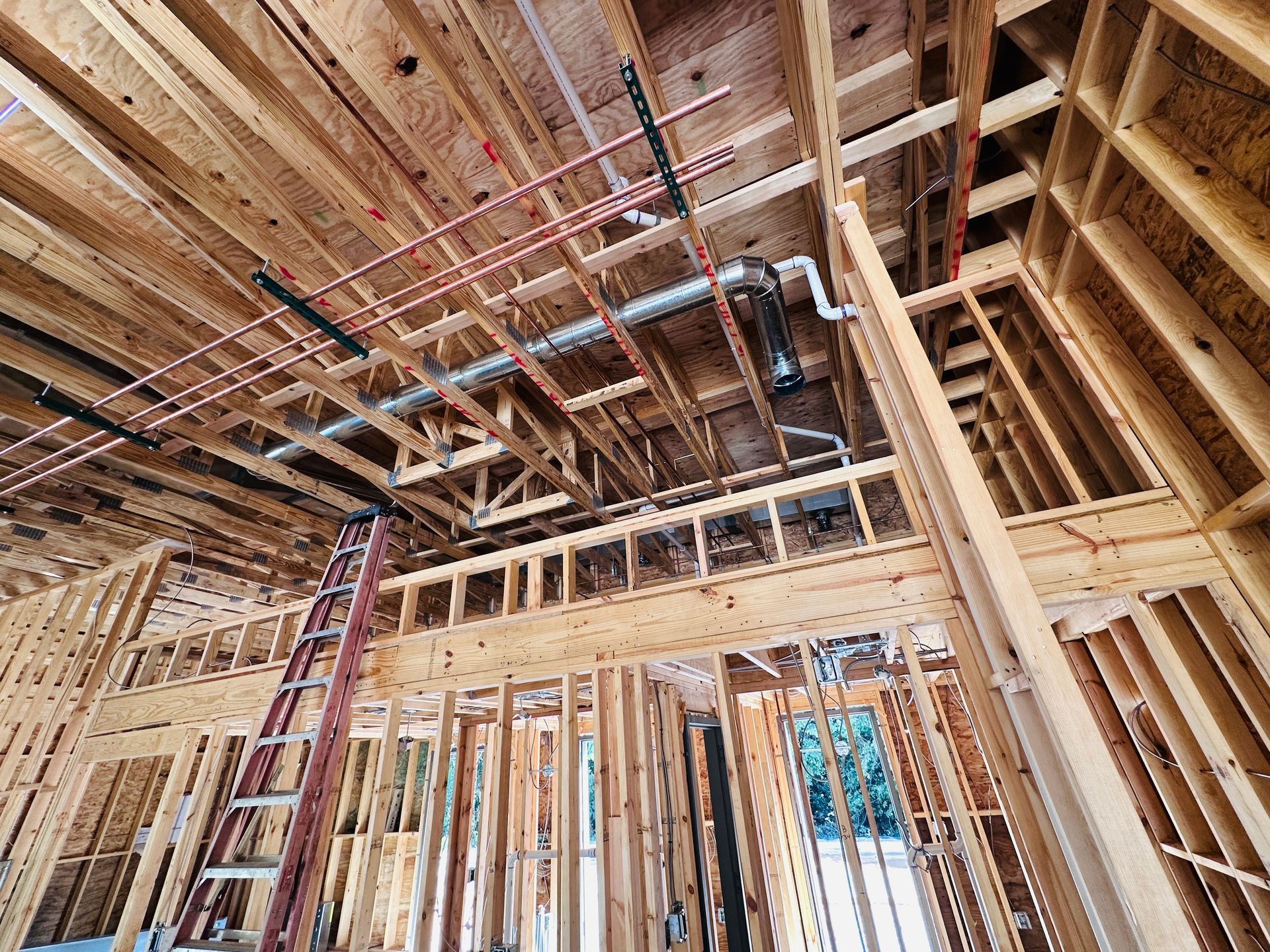 Framed house interior under construction with exposed wood beams, rafters, and a ladder