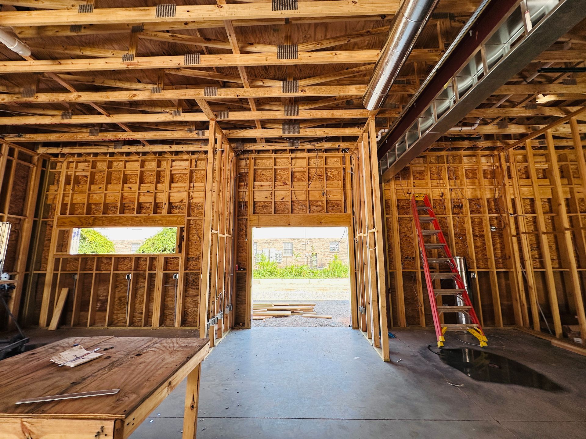 Interior of a partially framed garage with exposed studs, rafters, a red ladder, and open doorway
