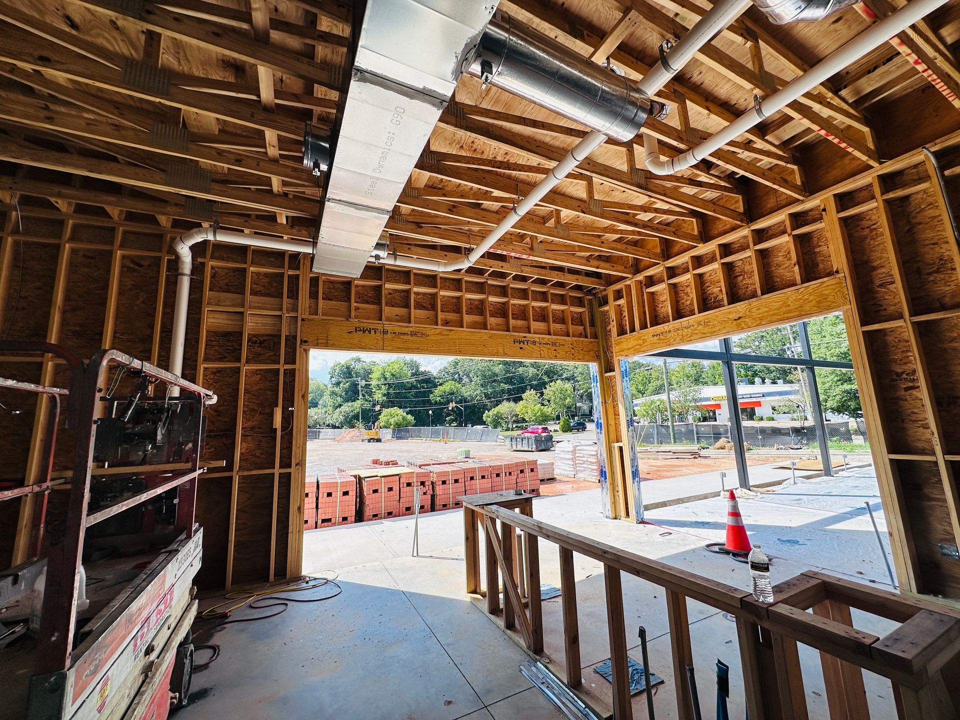 Construction site interior with exposed wooden framing and a view through a large opening to the street outside