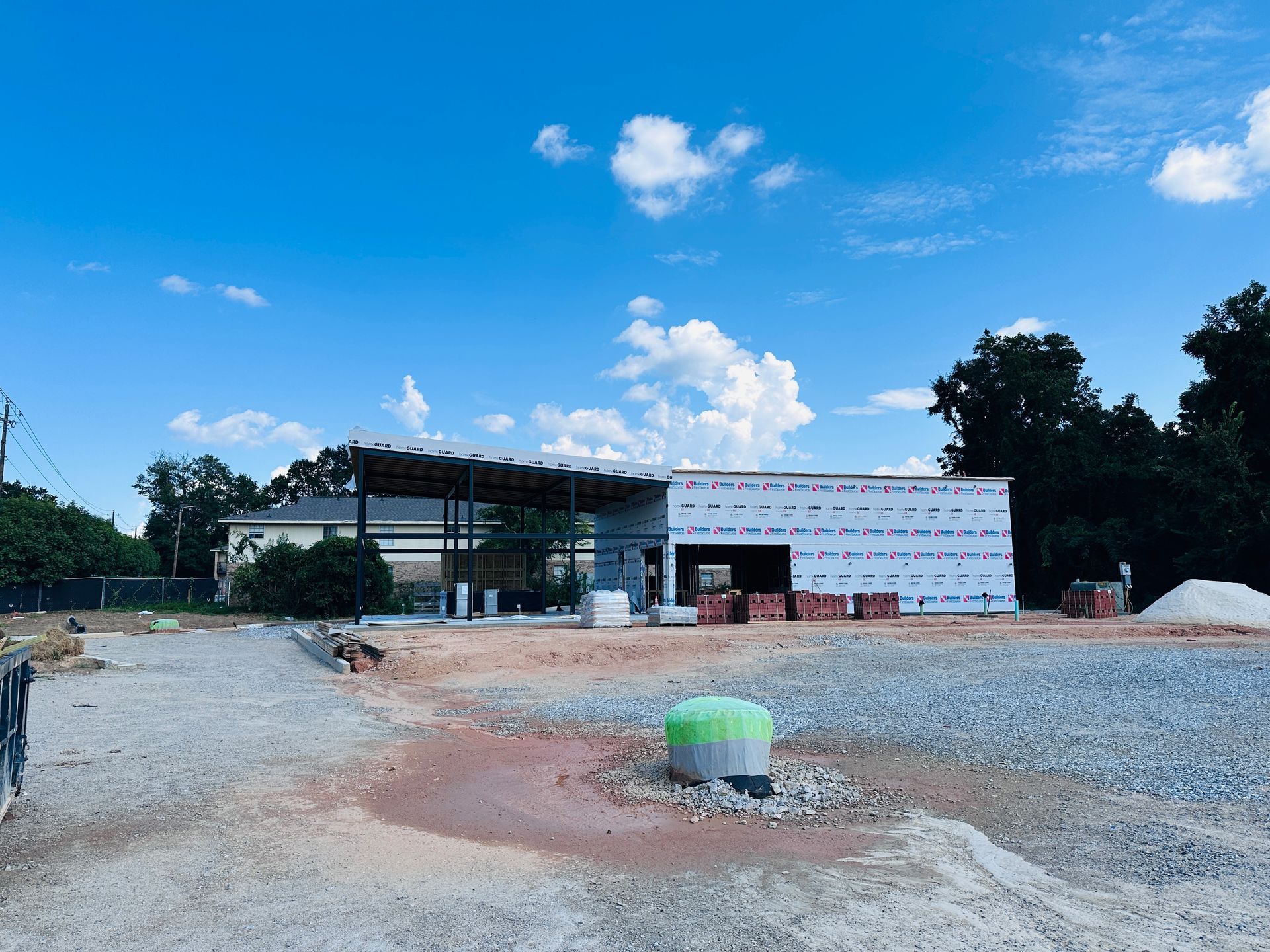 Construction site with gravel yard, unfinished building, and blue sky with clouds