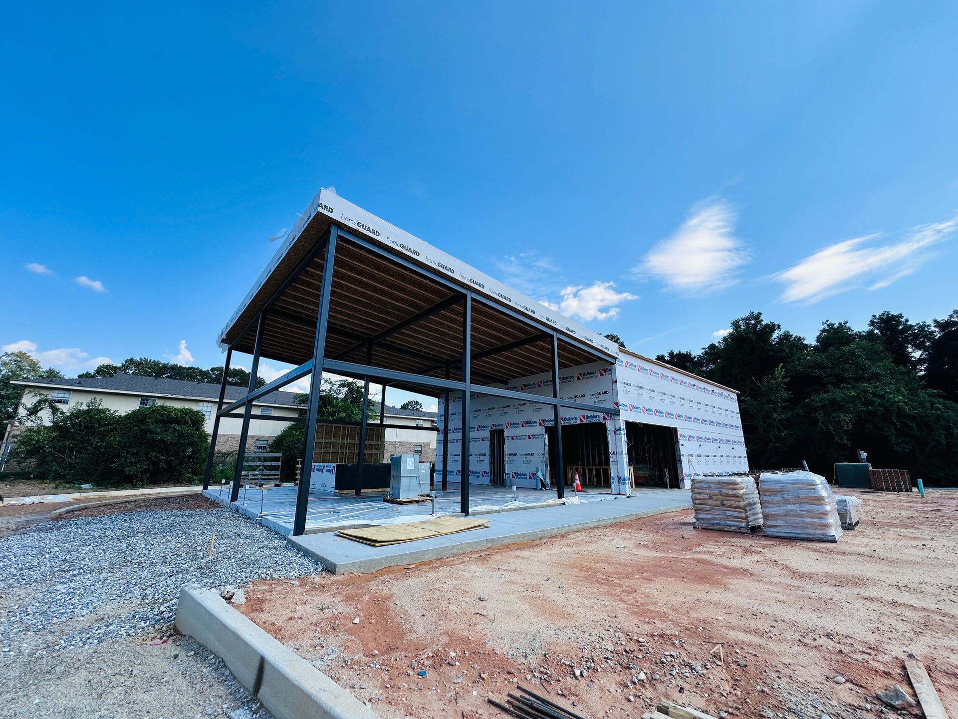 Open-air construction site with a steel-framed shelter and unfinished white building under a blue sky