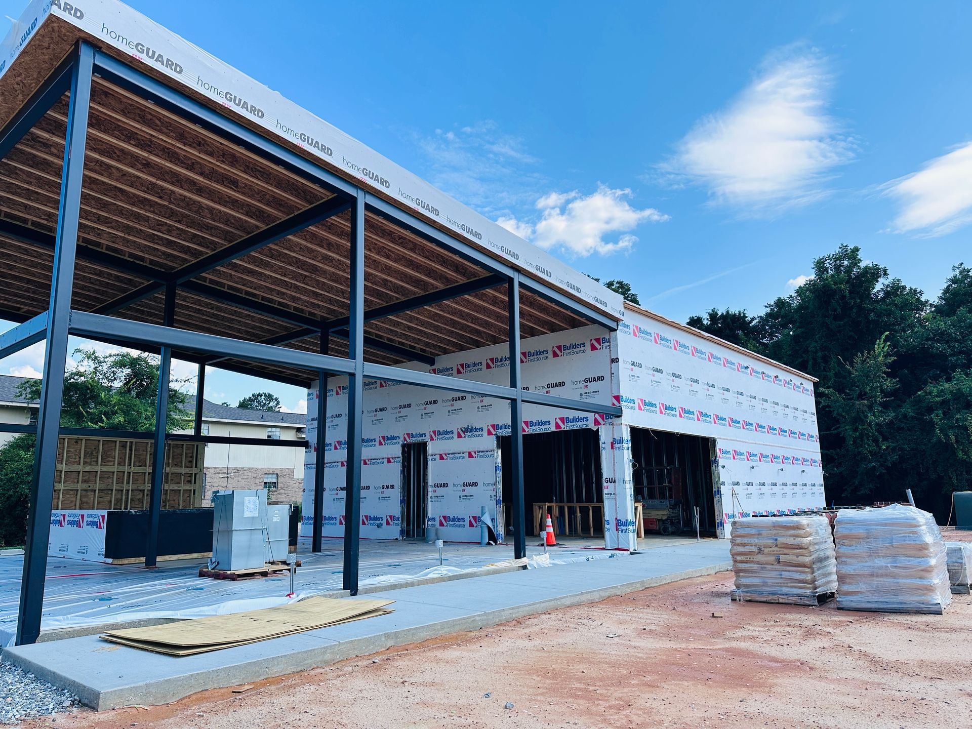 Partially built industrial warehouse with steel frame, white wall panels, and stacks of materials outside