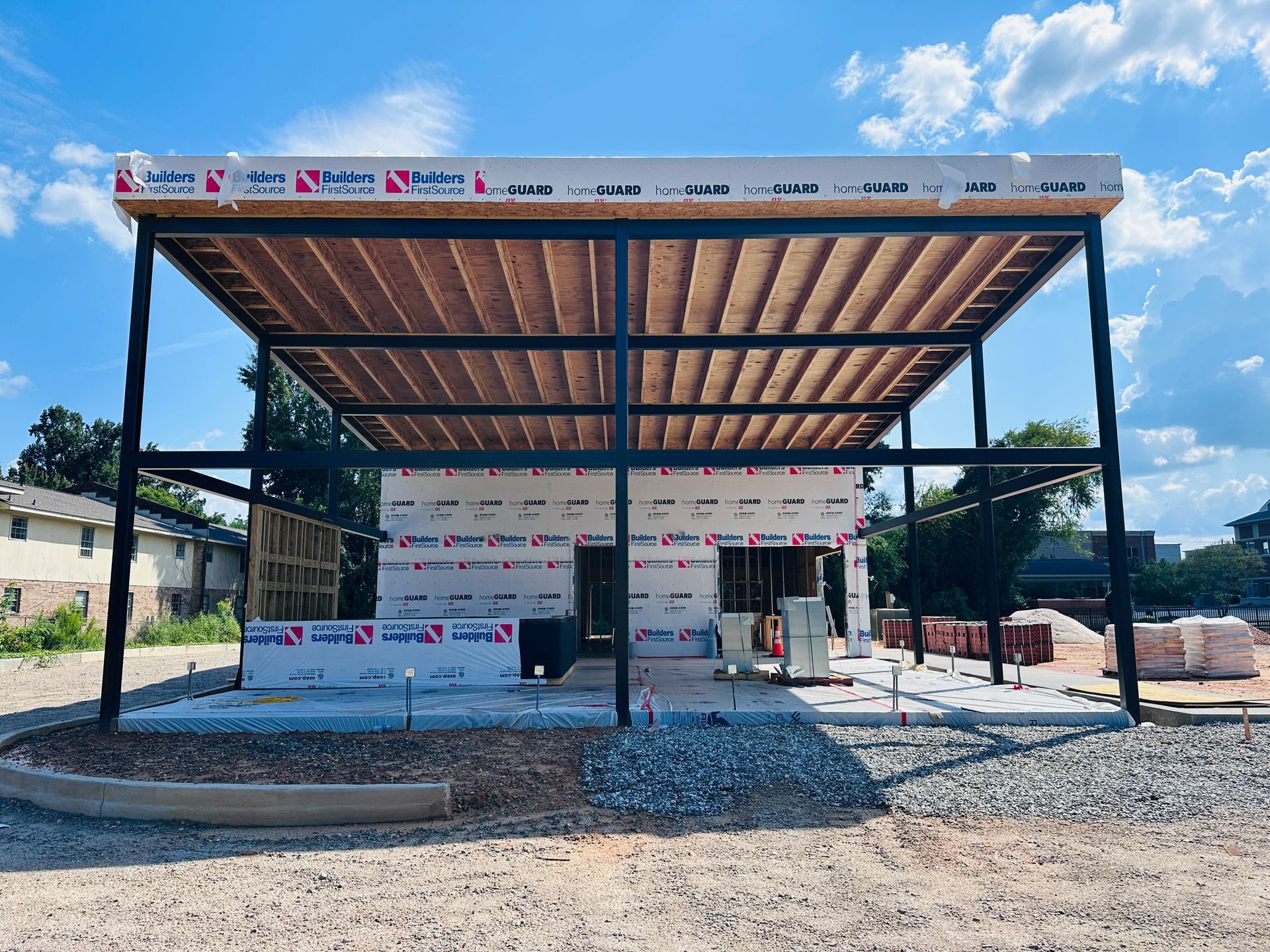 Open steel pavilion under construction with a brown roof and unfinished walls on a gravel lot.