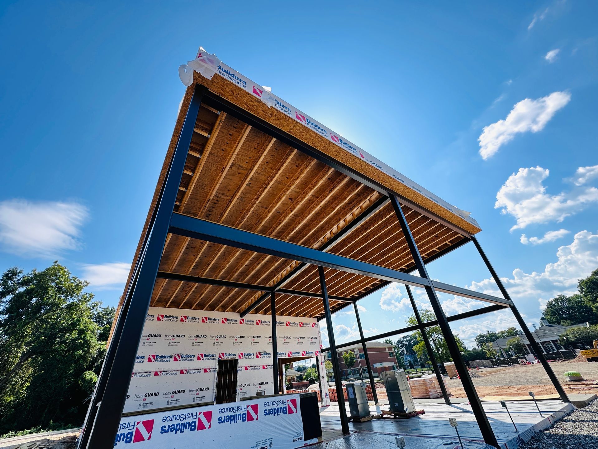 Open-air stage with a slanted wooden roof under a bright blue sky, in a construction or event area
