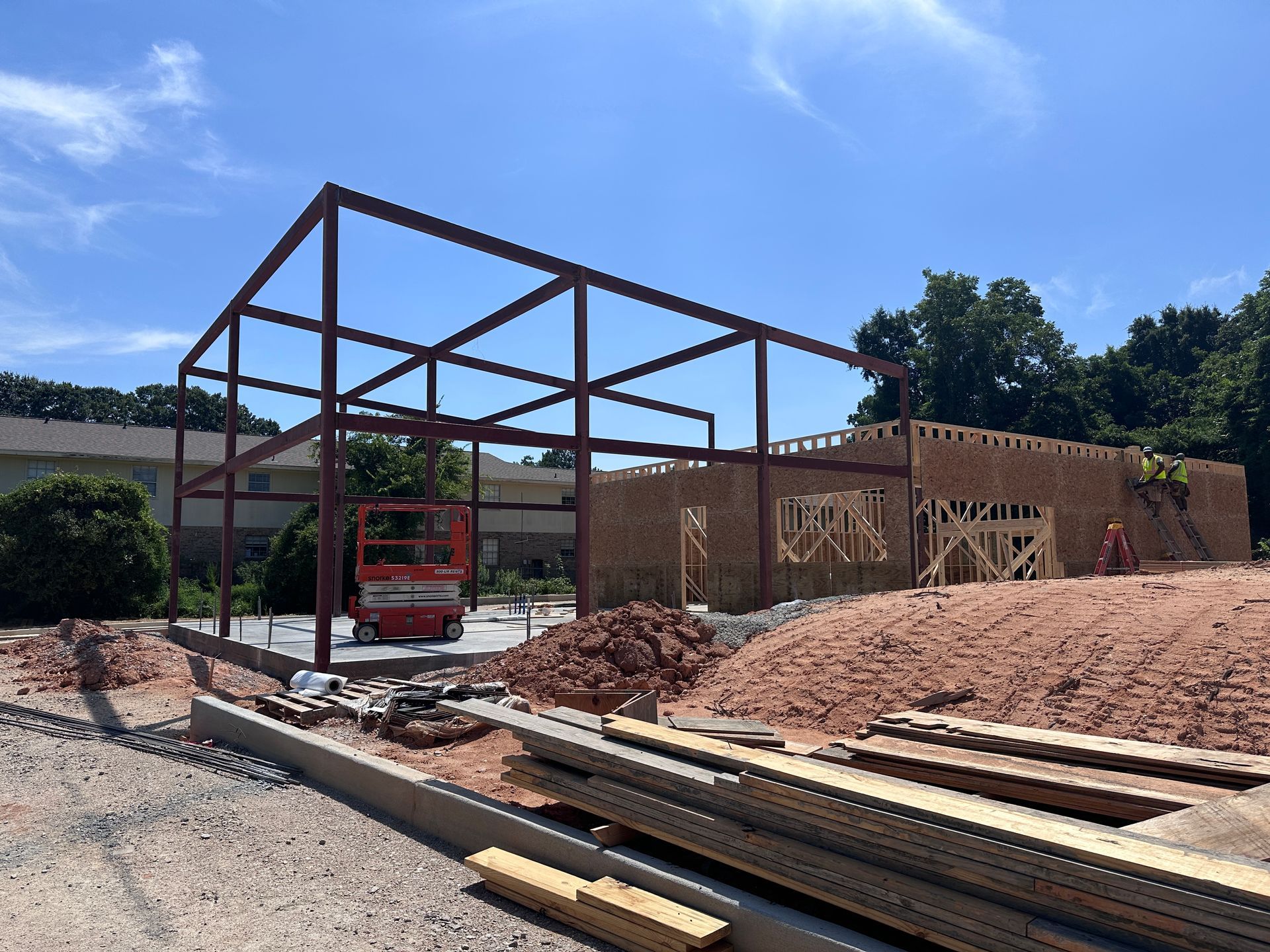 Construction site with steel frame, red lift, and lumber under a blue sky