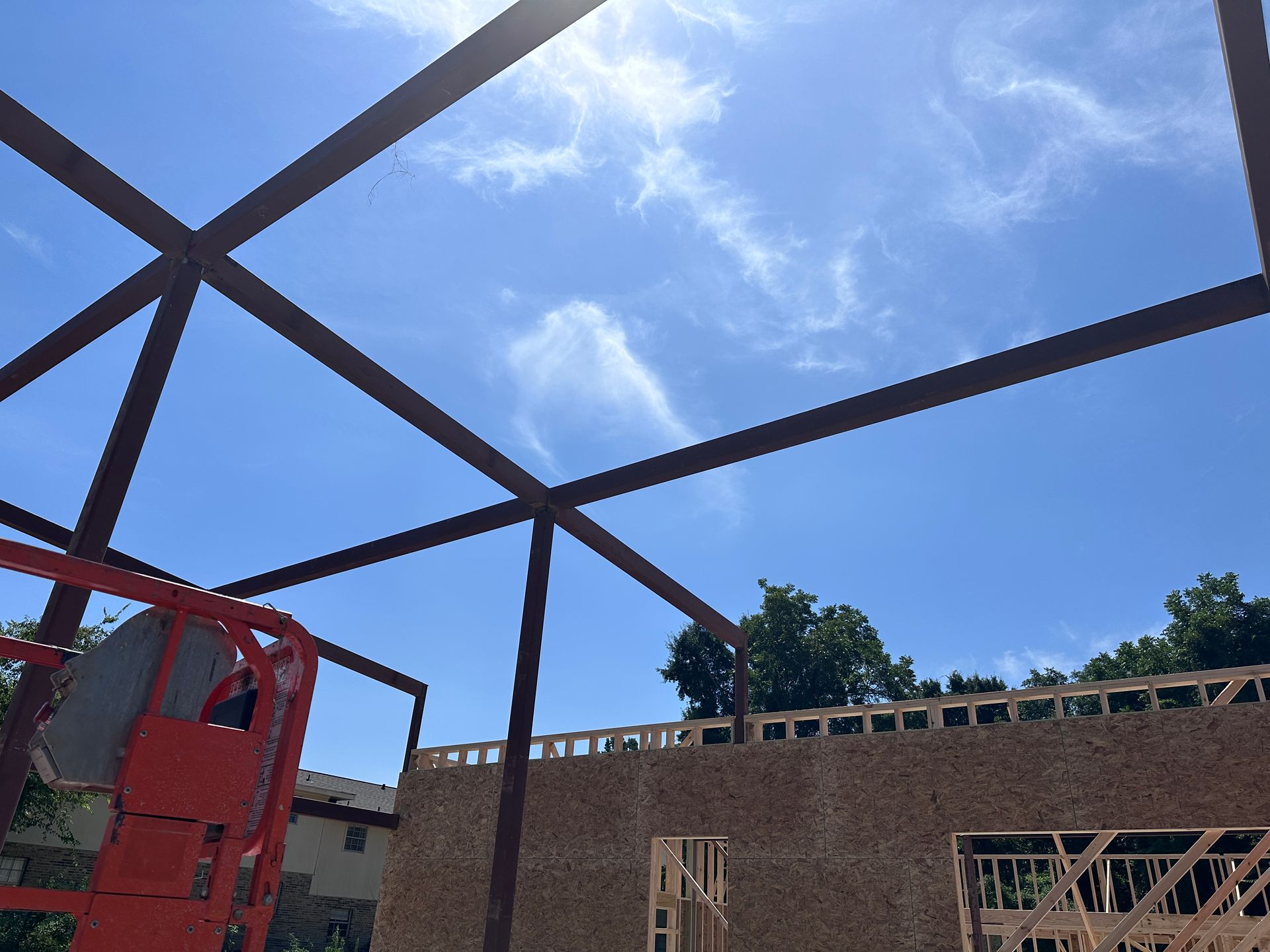 Partially built structure with metal roof frame under a blue sky and clouds