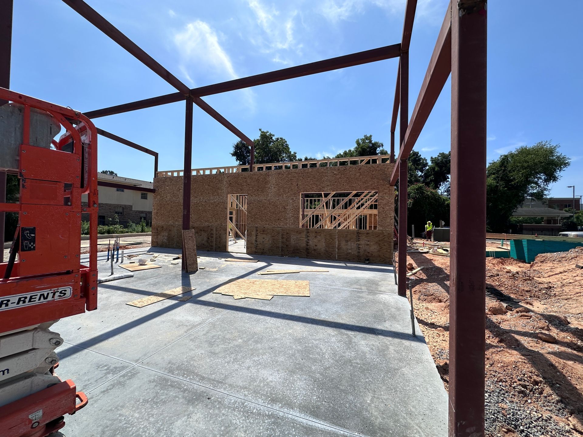 Steel frame construction on a concrete slab beside a partially built brick structure under a clear sky
