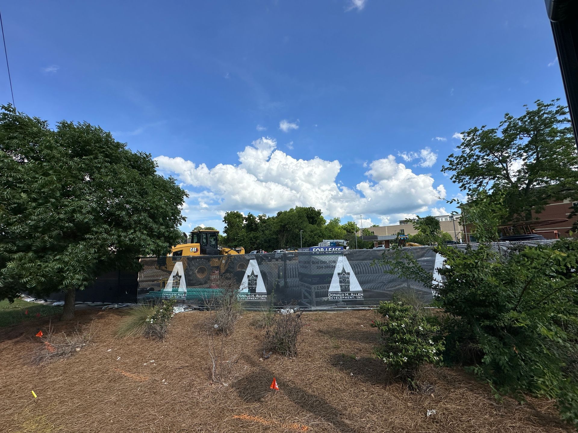 Construction site with white house-shaped barriers, yellow equipment, dirt foreground, and blue sky with clouds
