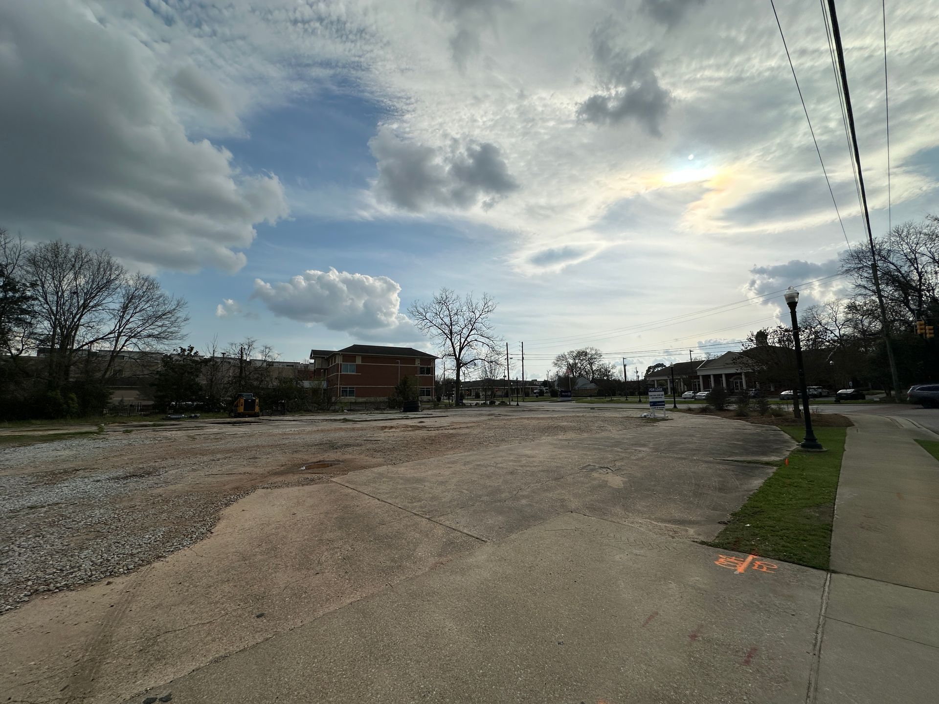 A wide view of a vacant, gravel-covered lot under a cloudy sky next to a sidewalk and a streetlight.