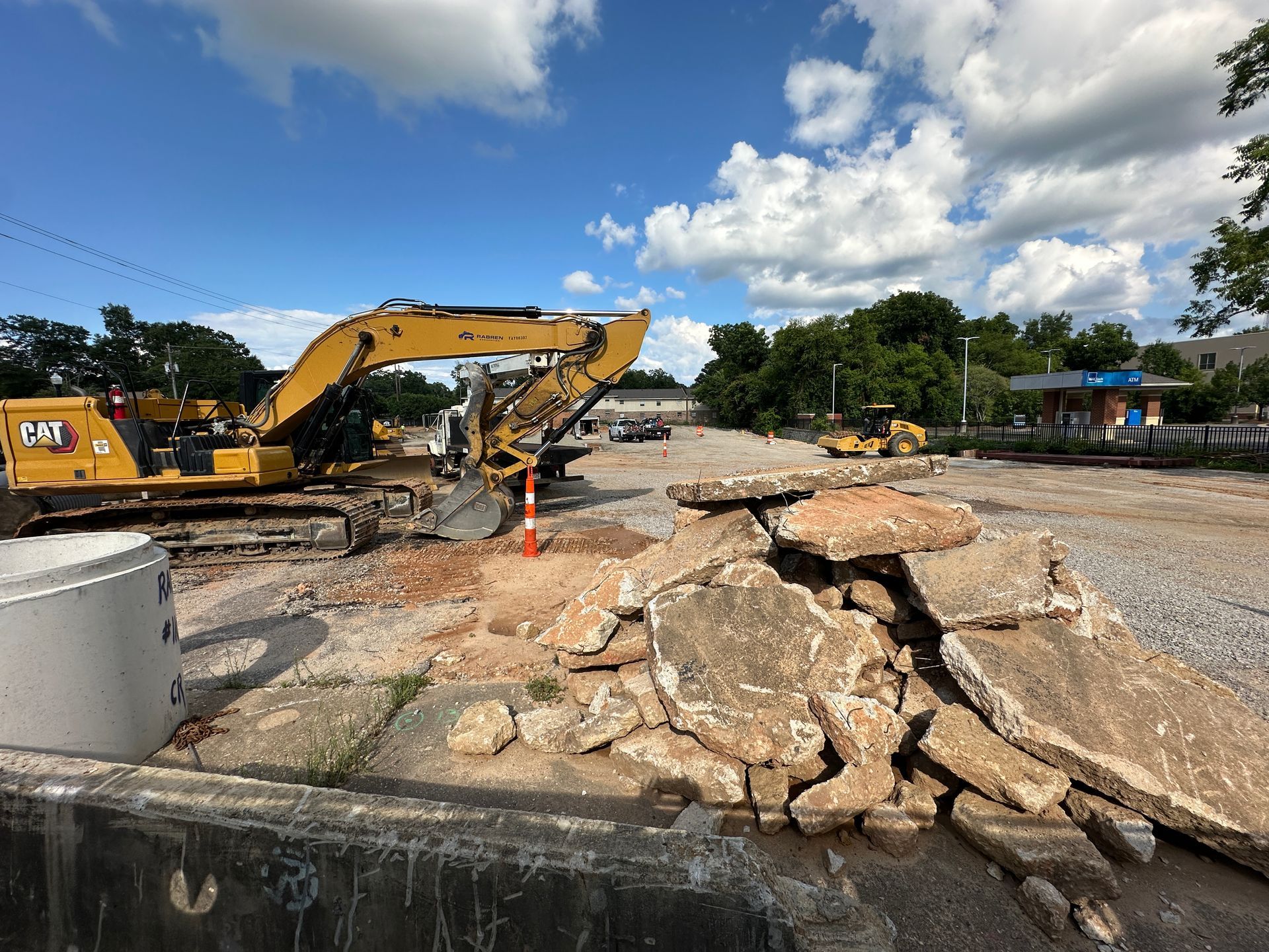 Yellow excavator clearing rubble on a damaged road under a blue sky