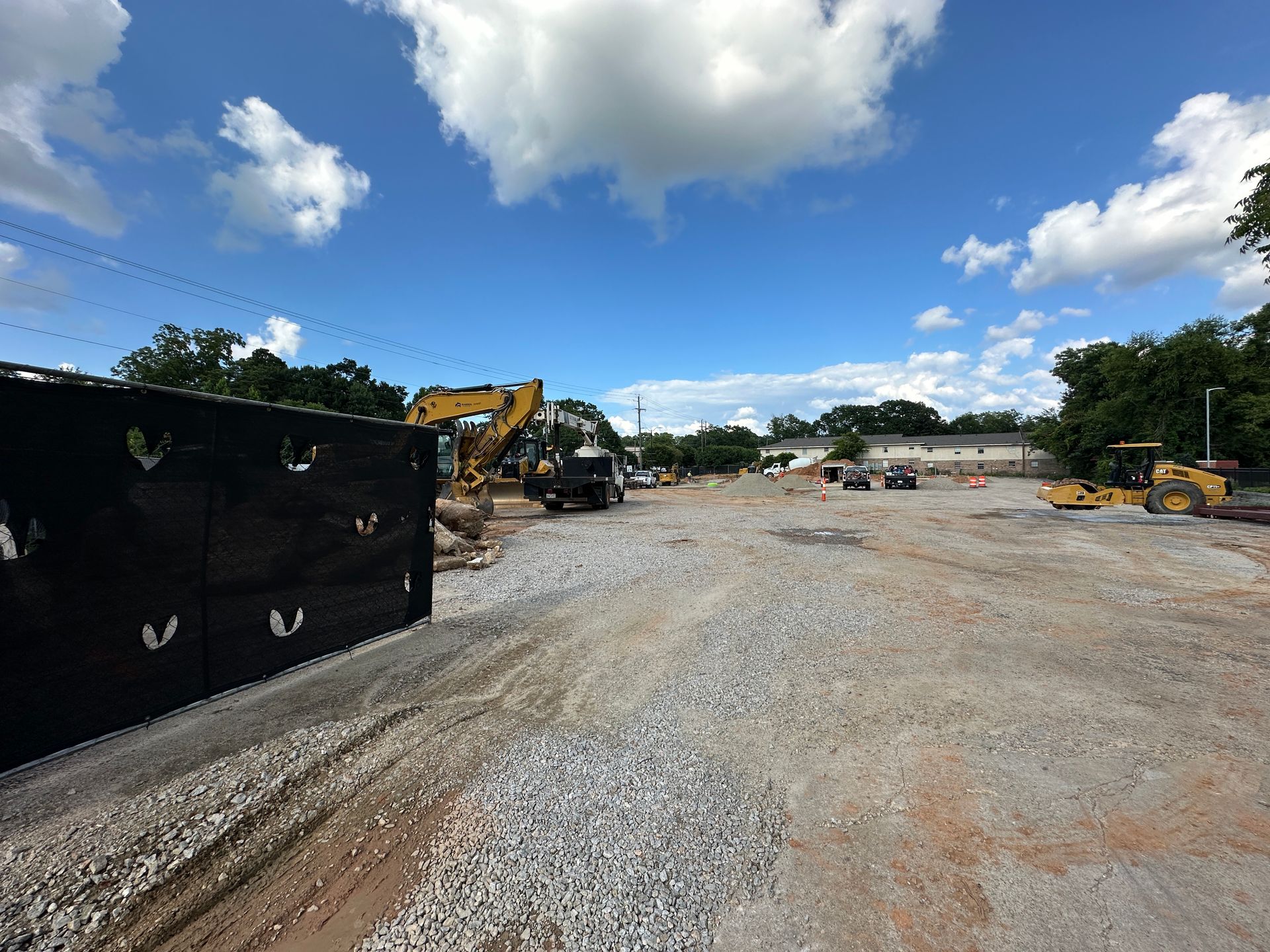 Construction site with gravel road, excavators, trucks, and a partly cloudy blue sky